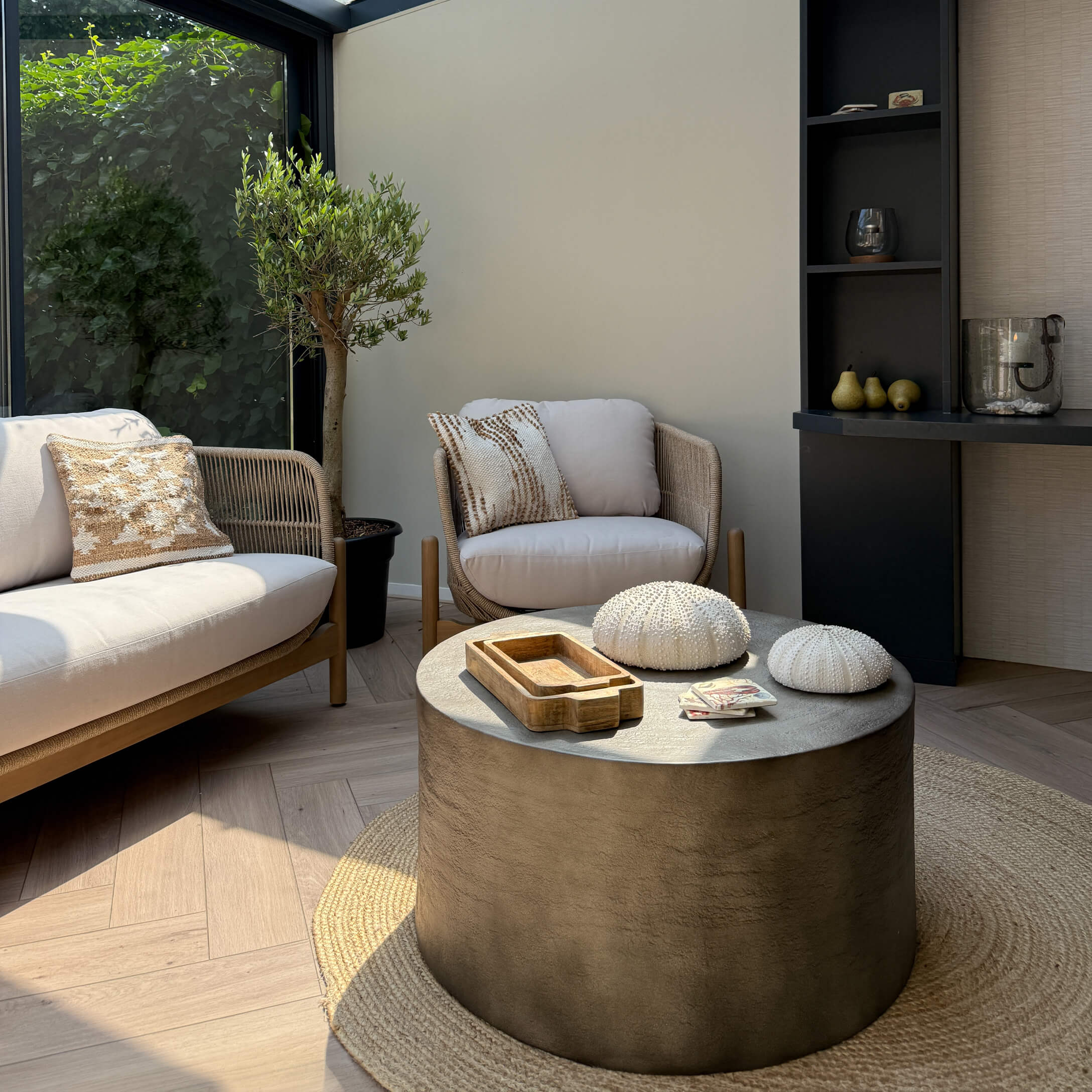 Moderner Wohnraum mit beigem Sofa und Sessel aus Stoff, runder Beton-Couchtisch auf Naturteppich