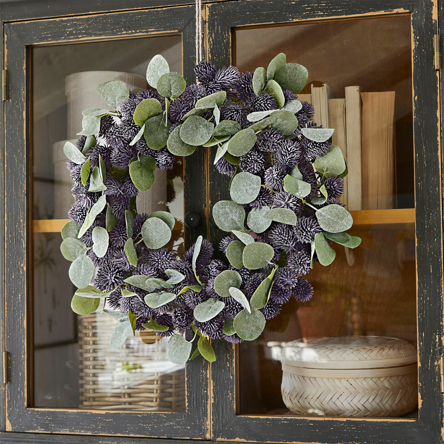 Kranz Épine Dekorativer Kranz mit grünen Blättern und violetten Kugeln an schwarzem Holzschrank