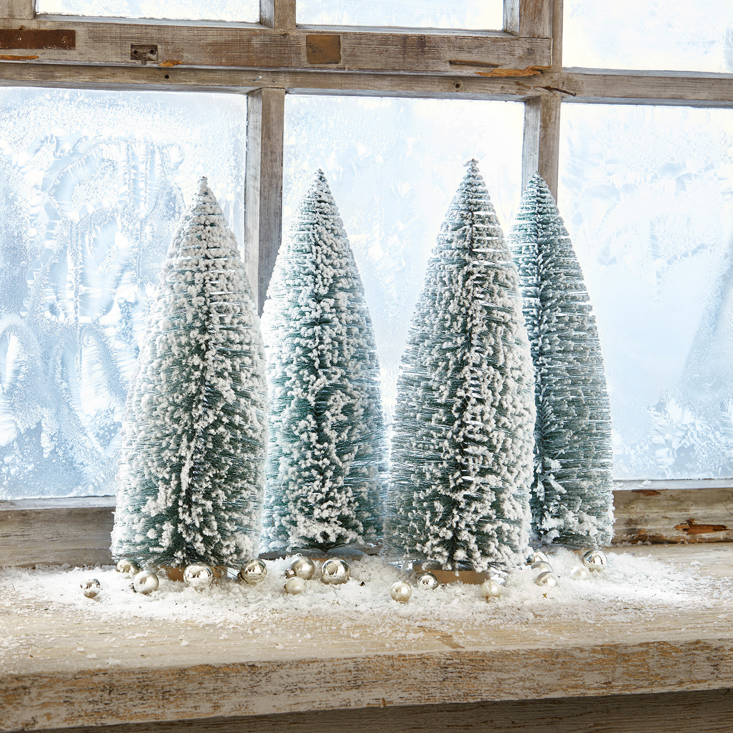 Deko-Baum 4er Set Landscape Vier grüne Kunststoff-Tannenbäume in Kegelform mit weissem Schnee auf einem Holzfensterbrett mit silbernen Kugeln