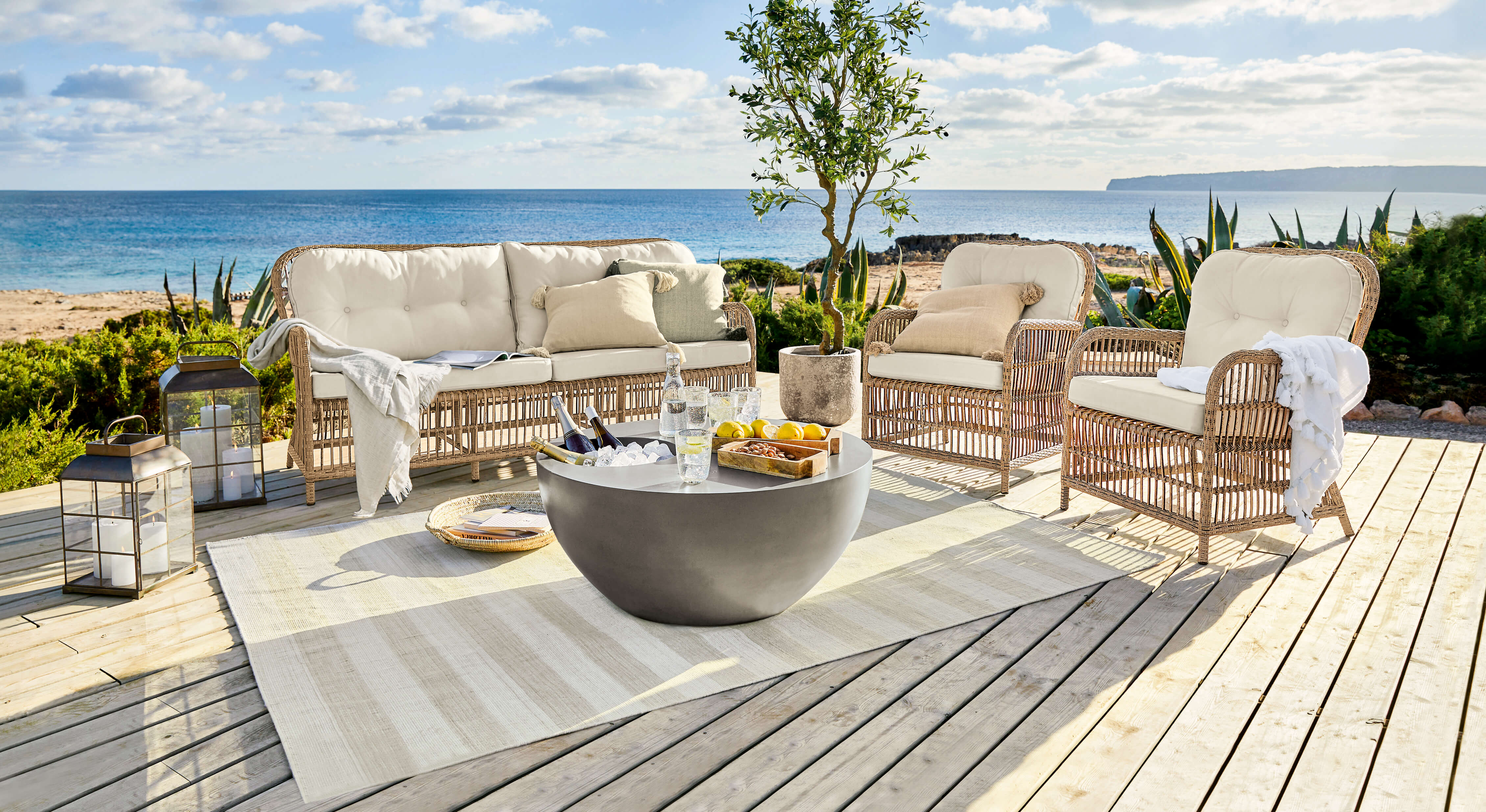 Rattan-Gartenmöbel-Set mit cremefarbenen Polstern auf Holzterrasse mit Meerblick
