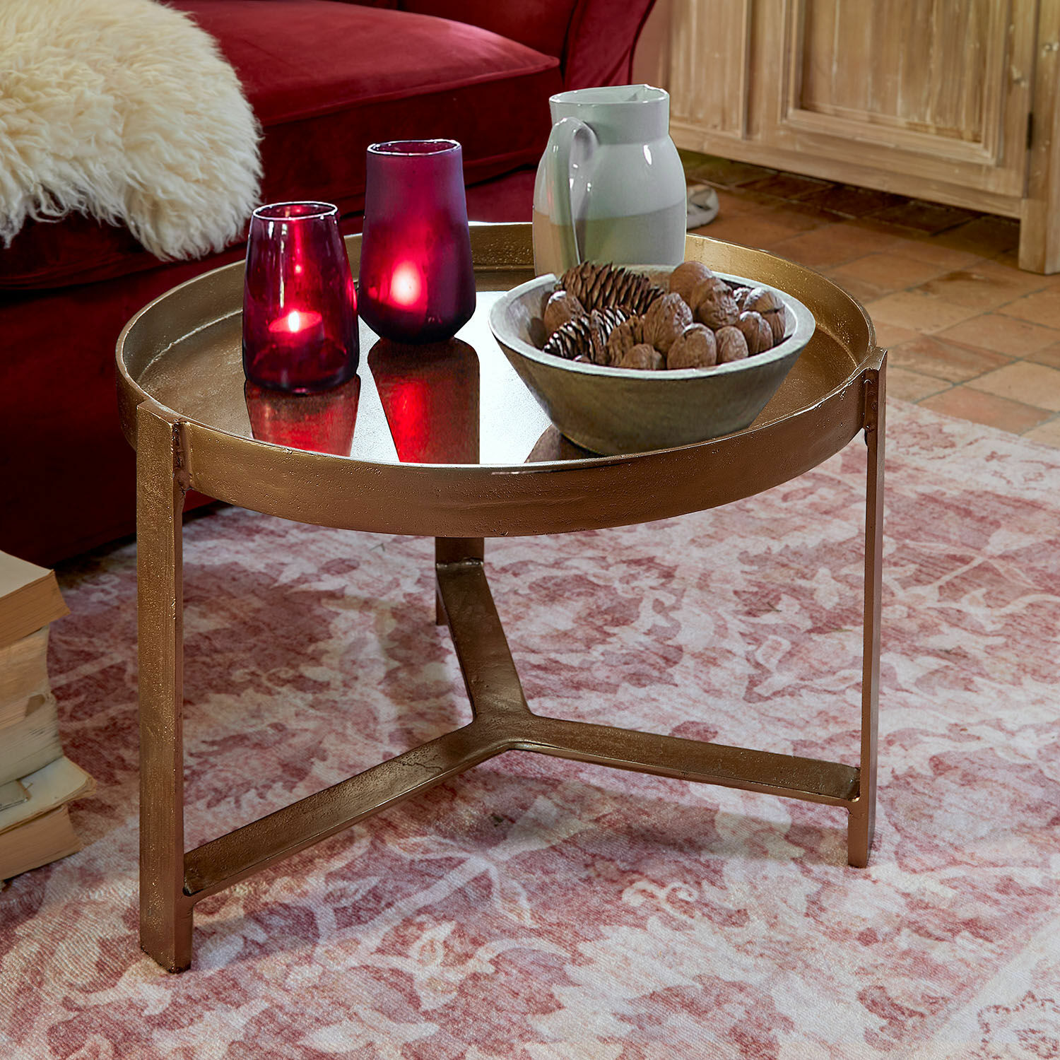 Couchtisch Mirouette Runder Couchtisch aus Metall in Kupferfarbe auf rosa Teppich mit dekorativen Kerzen und Schale