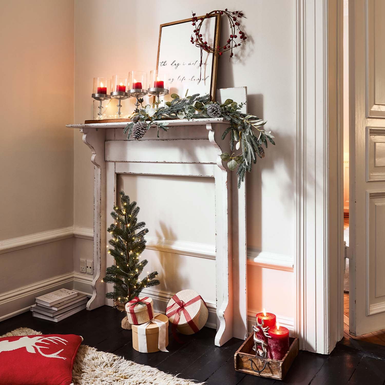 Weißer Holz-Kamin mit Weihnachtsdekoration, roten Kerzen und verpackten Geschenken auf dem Boden