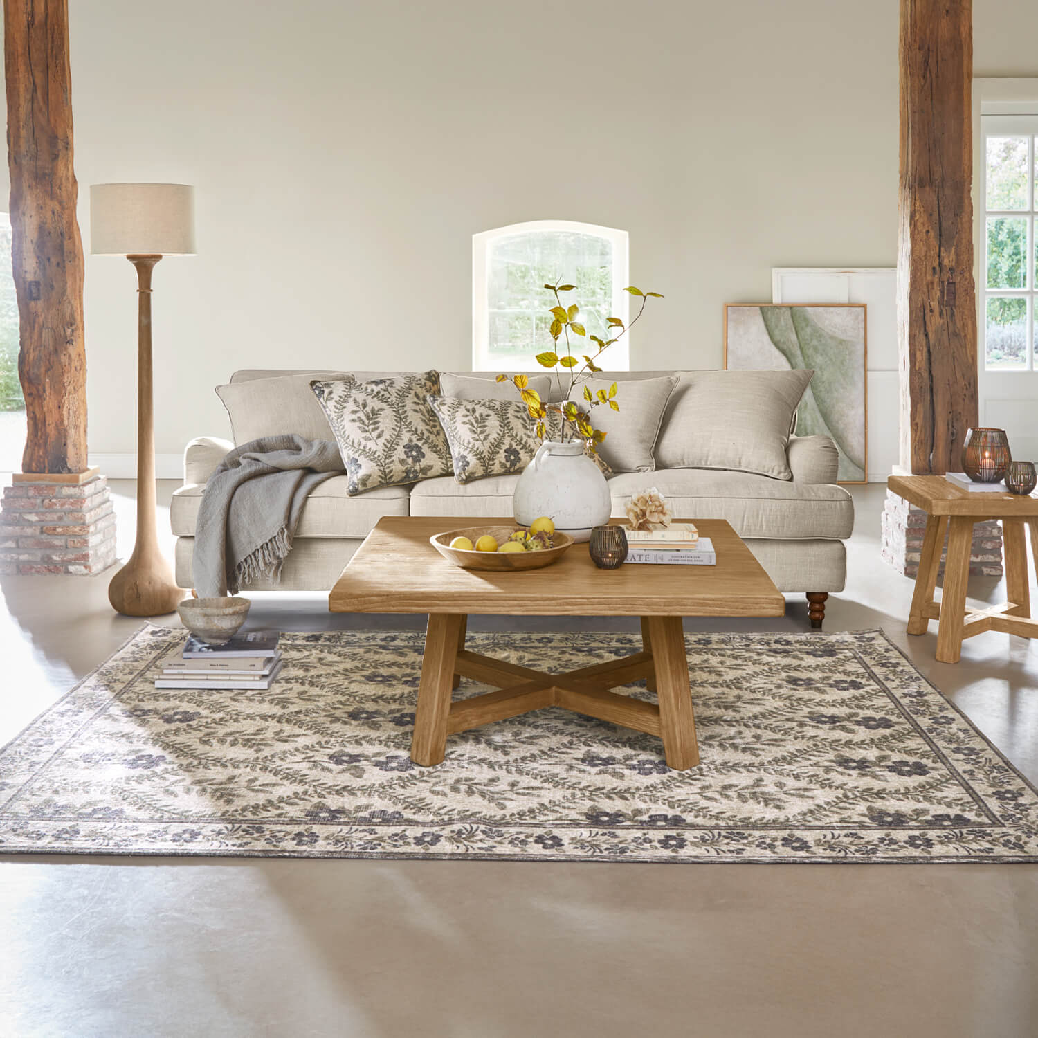 Gemütliches Wohnzimmer mit beigem Sofa, Holzcouchtisch und floral gemustertem Teppich