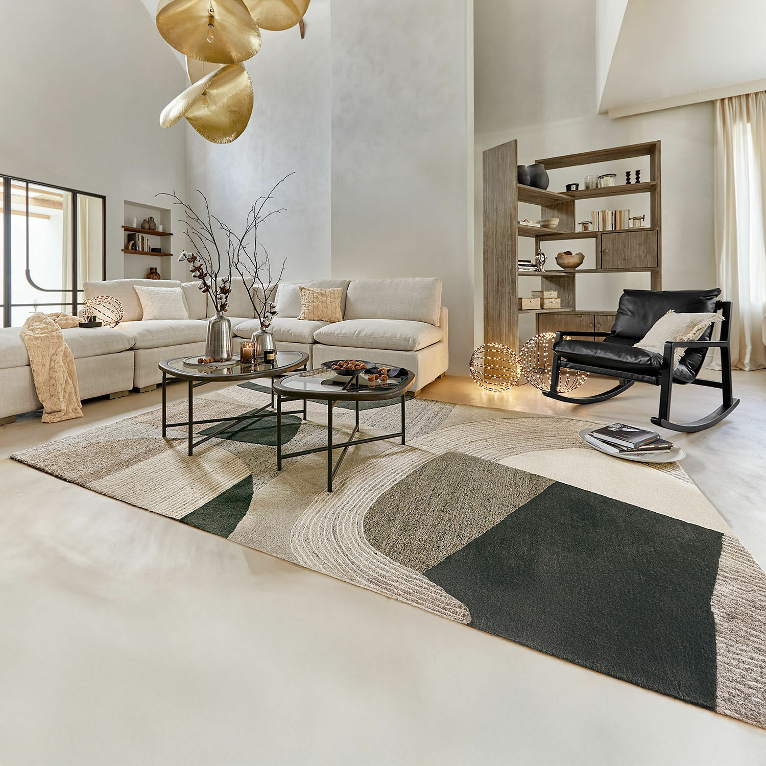 Teppich Kembria Moderner Wohnraum mit beigem Sofa, schwarzem Schaukelstuhl und geometrischem Teppich in Naturtönen