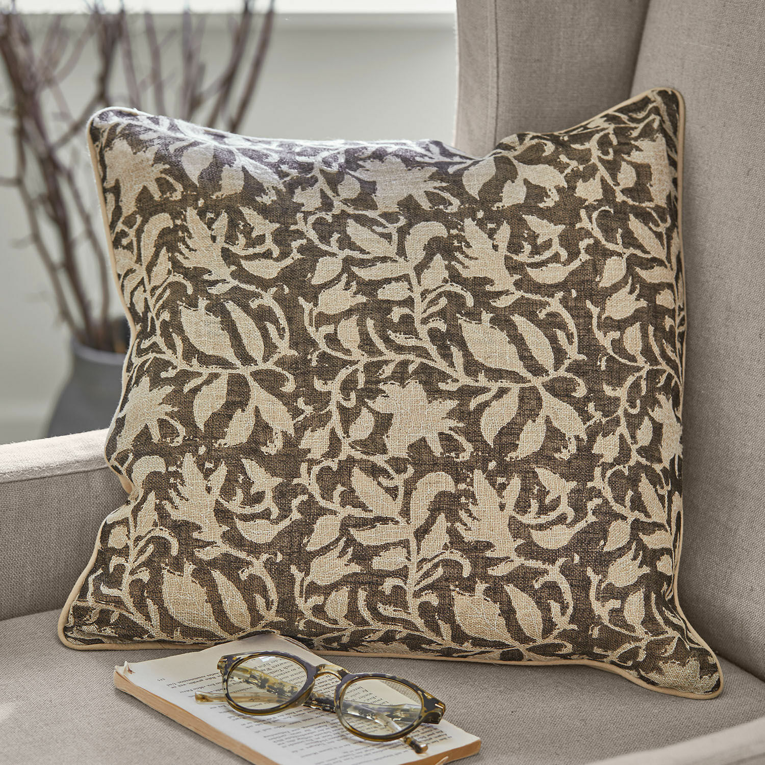 Kissenhülle 2er Set Ziradayn Braun-beiges Baumwollkissen mit Pflanzenmuster auf grauem Sofa mit Brille und Buch