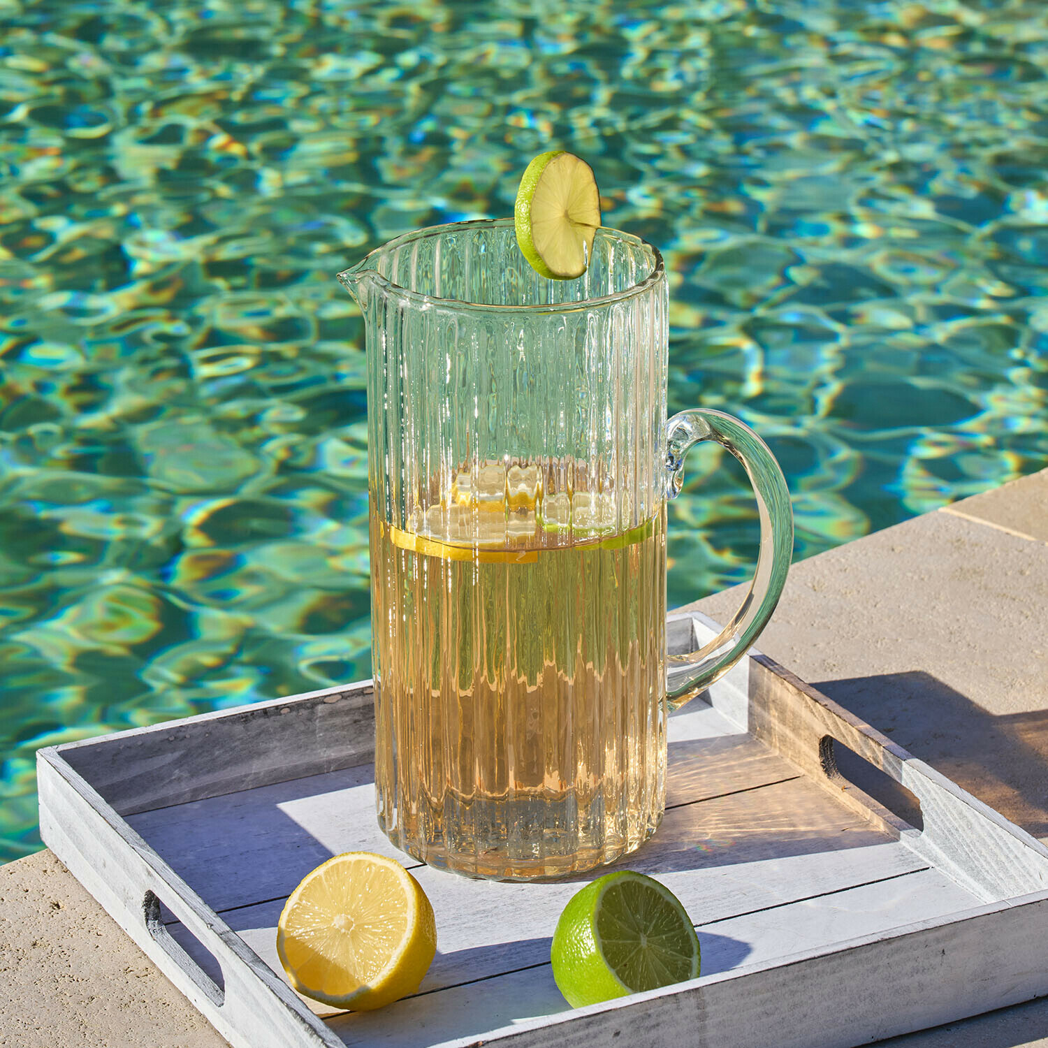 Krug Solerón Transparenter Glas-Krug mit Getränk und Limettenscheibe auf weissem Tablett am Poolrand