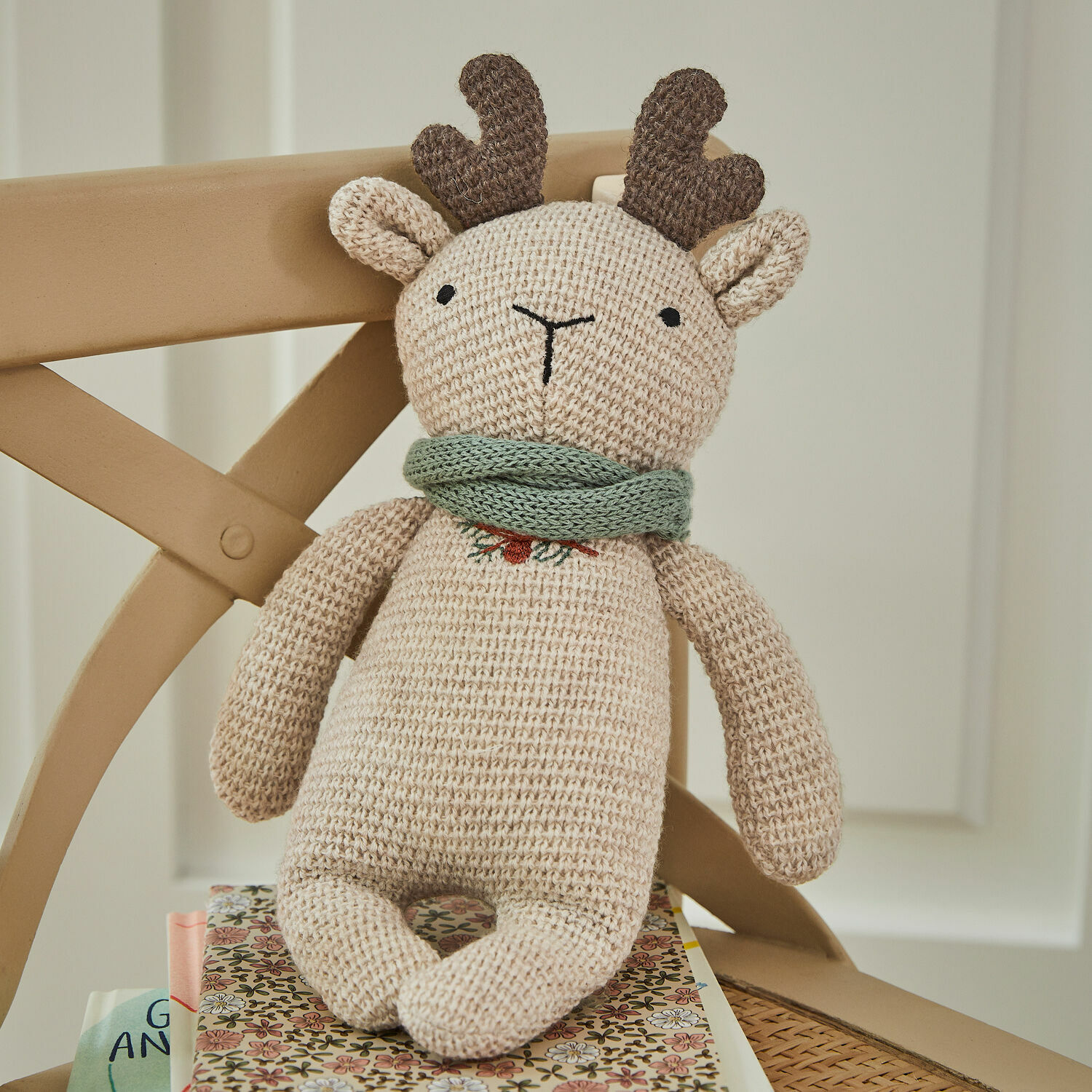 Stofftier Papillia Beiges gestricktes Rentier mit braunen Hörnern und grünem Schal, sitzend auf einem Stuhl
