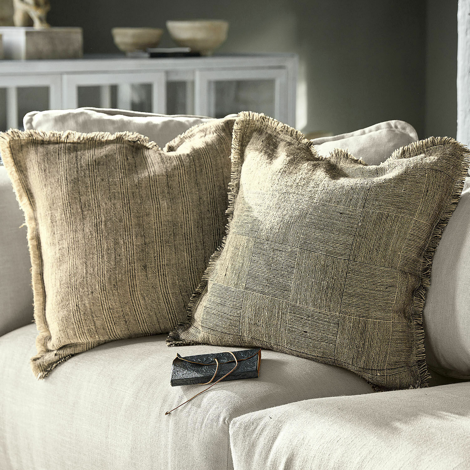 Kissenhülle 2er Set Amur Zwei beige dekorative Kissen mit Fransen auf einem hellgrauen Sofa im modernen Wohnzimmer