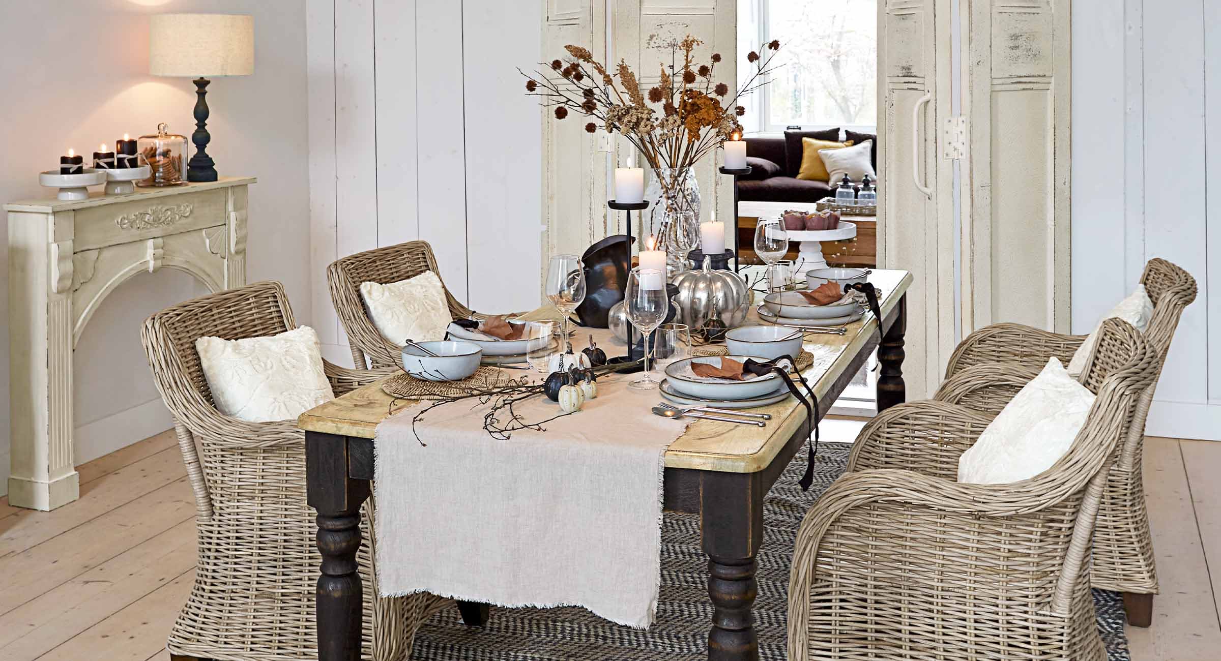 Esszimmer mit Rattanstühlen und Holztisch, dekoriert mit Kerzen und herbstlichen Accessoires