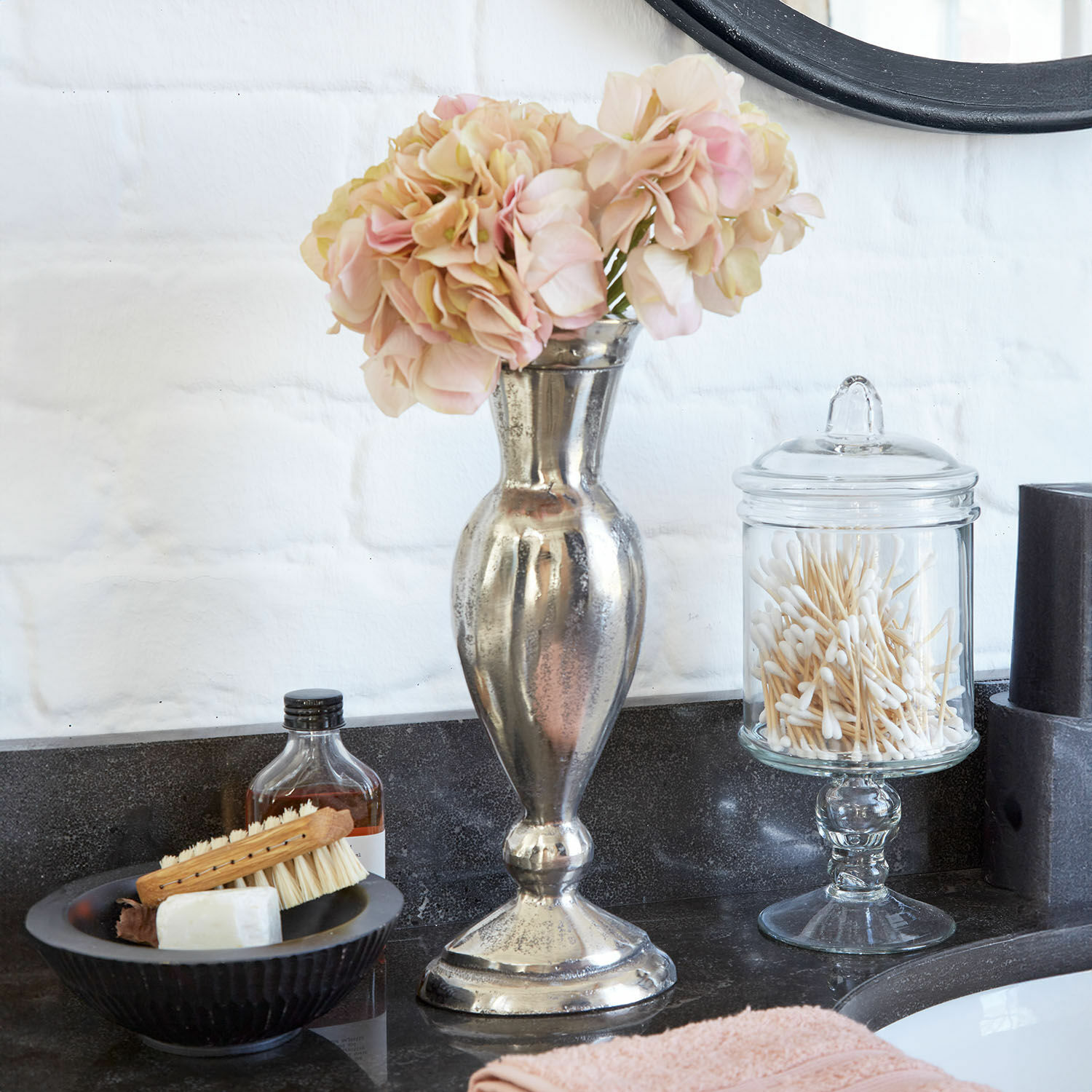 Vase Carvella Silberne Metallvase mit rosa Blumen auf schwarzer Badezimmerablage mit Pflegeaccessoires