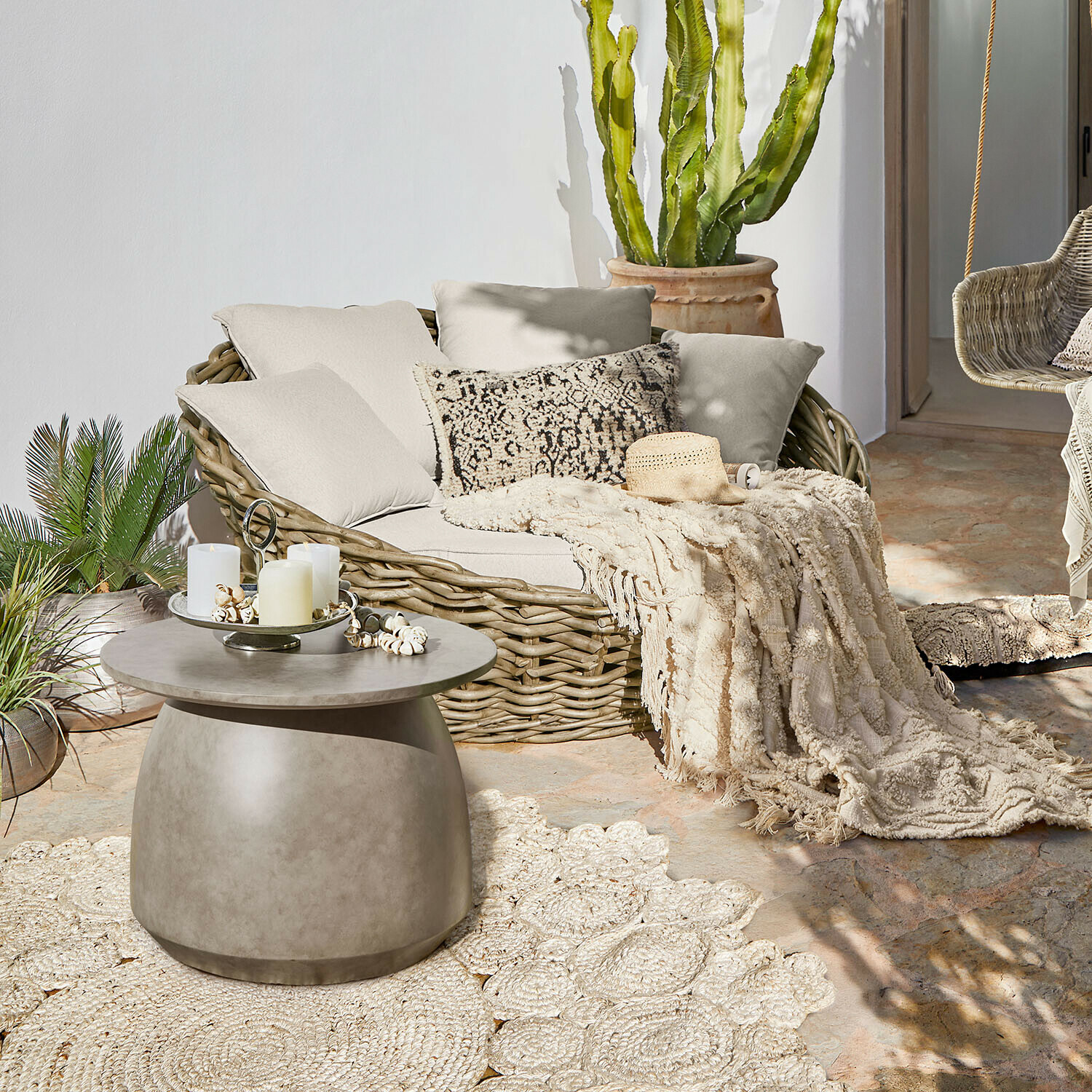Gartenlounge Varolinos Rundes Rattansofa mit cremefarbenen Kissen und Decke auf Terrasse mit Beton-Couchtisch
