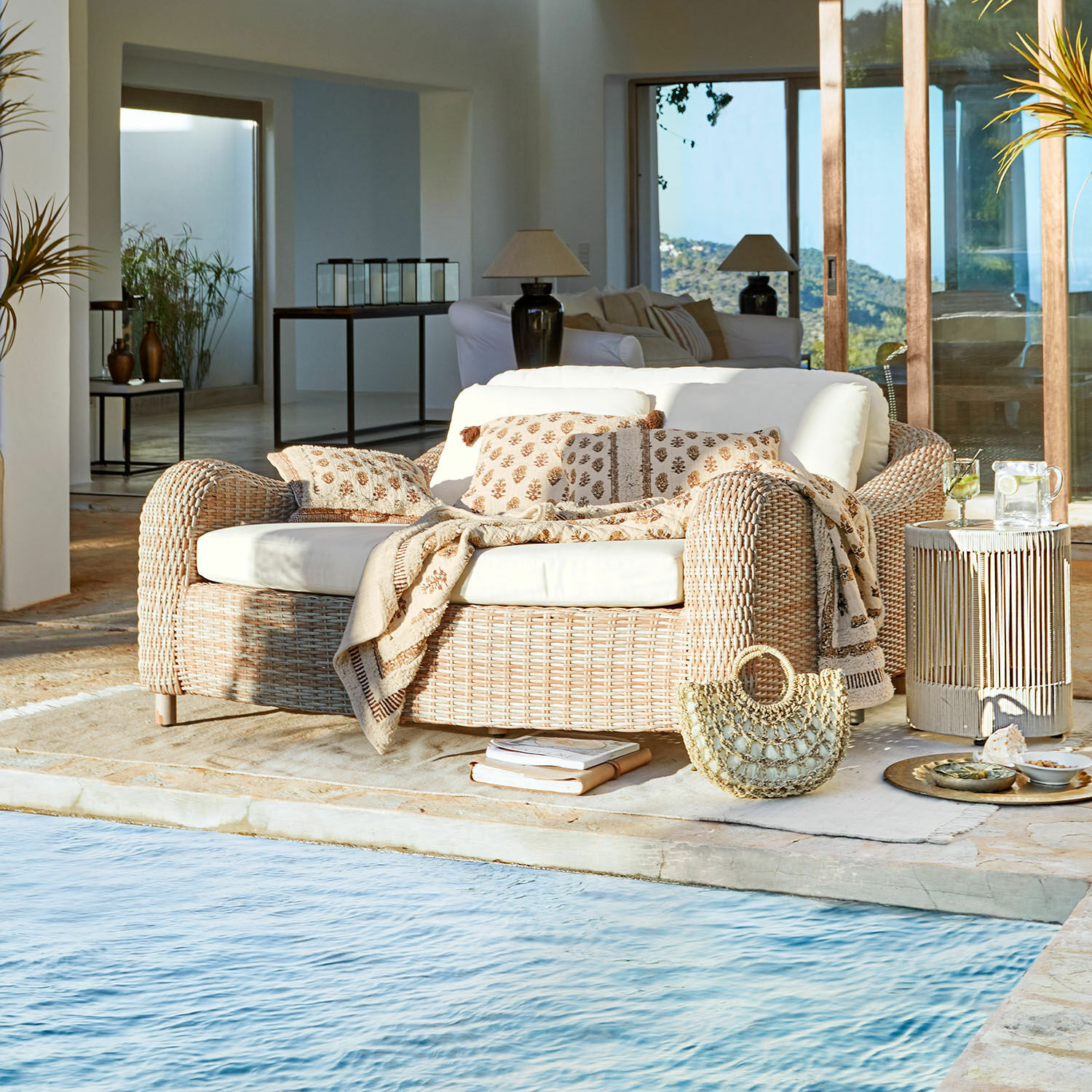 Lounger Heloite Natürliches Rattansofa mit cremefarbenen Kissen und Decke am Pool in modernem Wohnzimmer