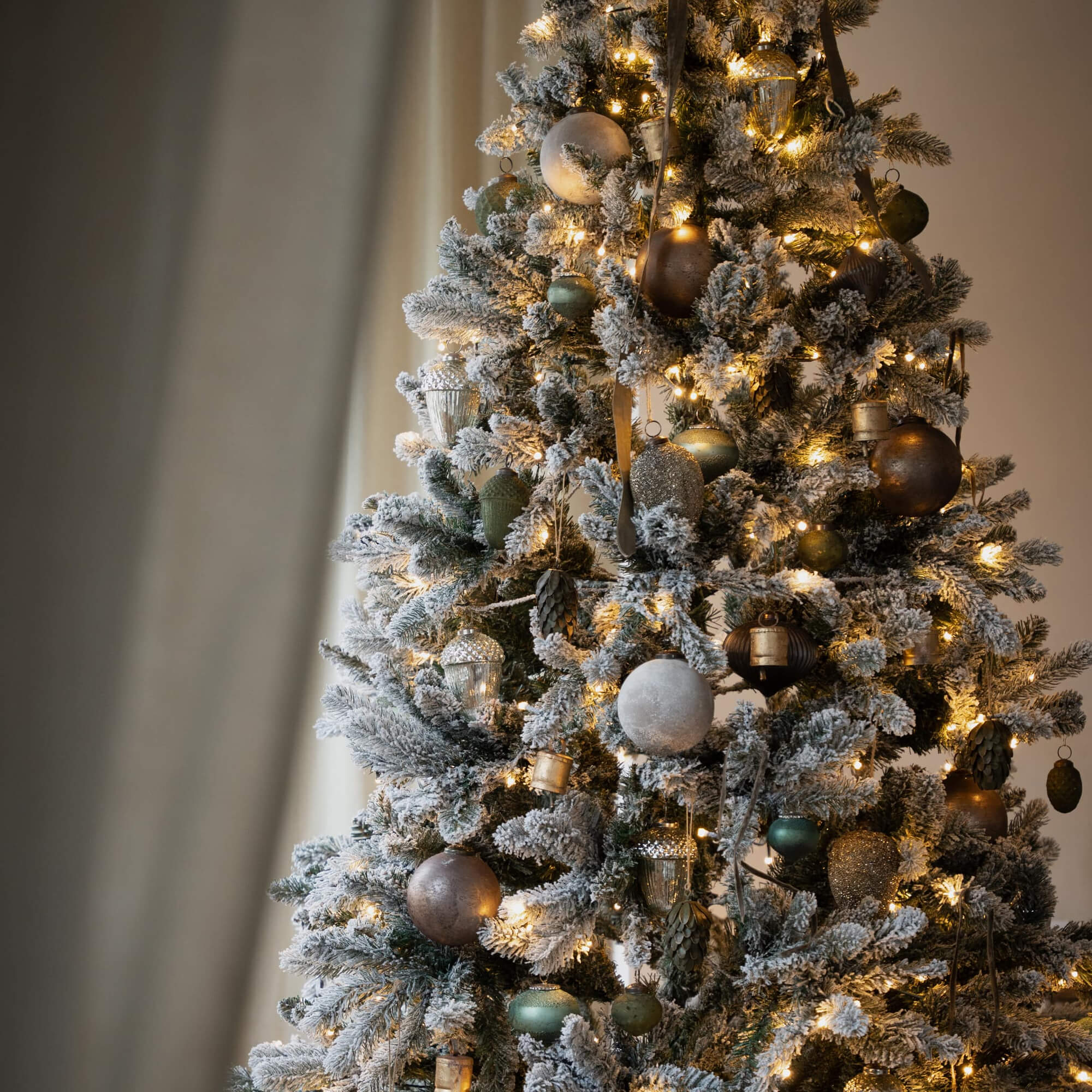 Künstlicher Weihnachtsbaum mit Schneeeffekt und goldgrünen Kugeln, beleuchtet für festliche Stimmung