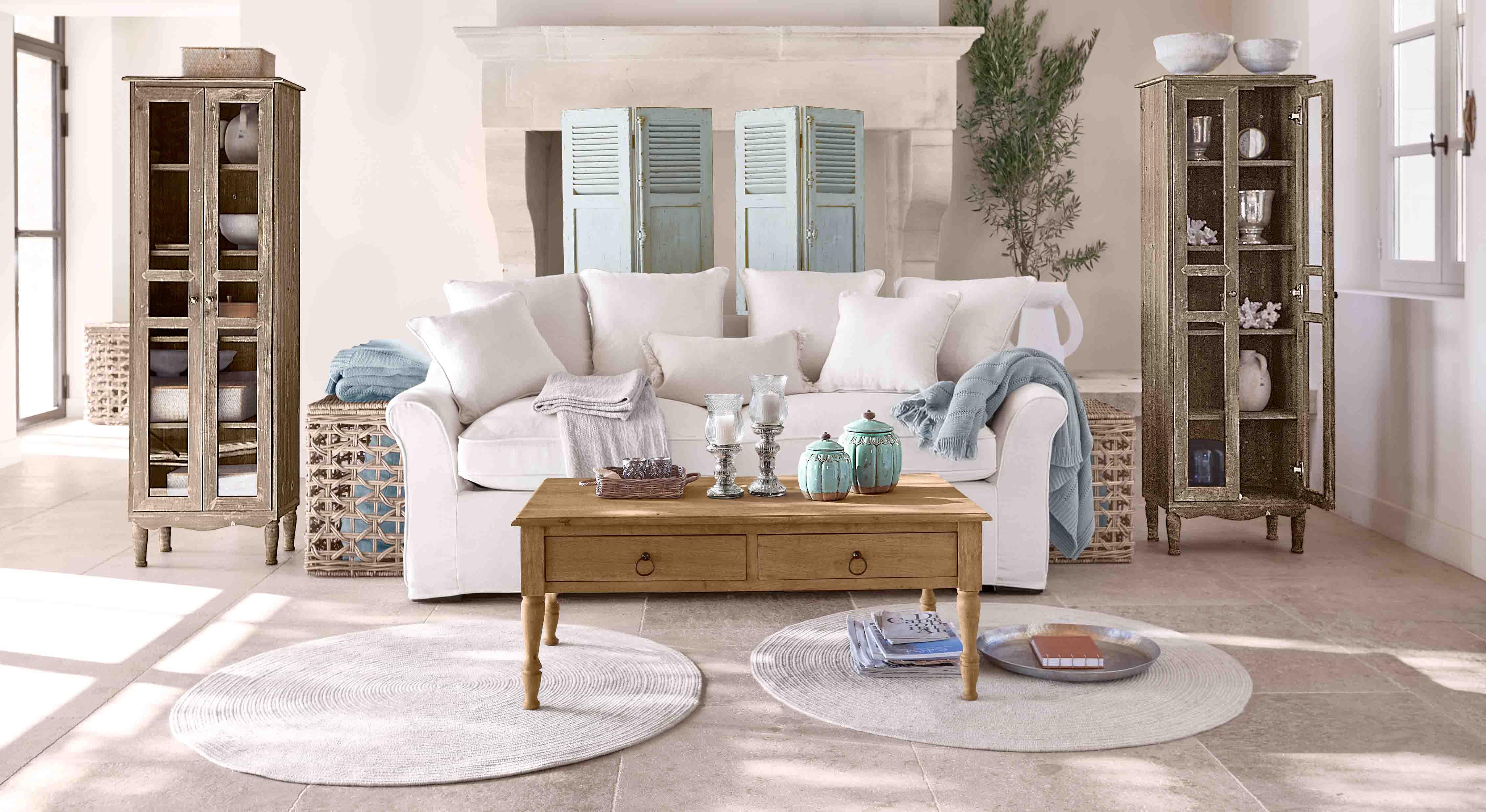 Gemütliches Wohnzimmer mit weissem Sofa, Holzcouchtisch und zwei antiken Holzvitrinen