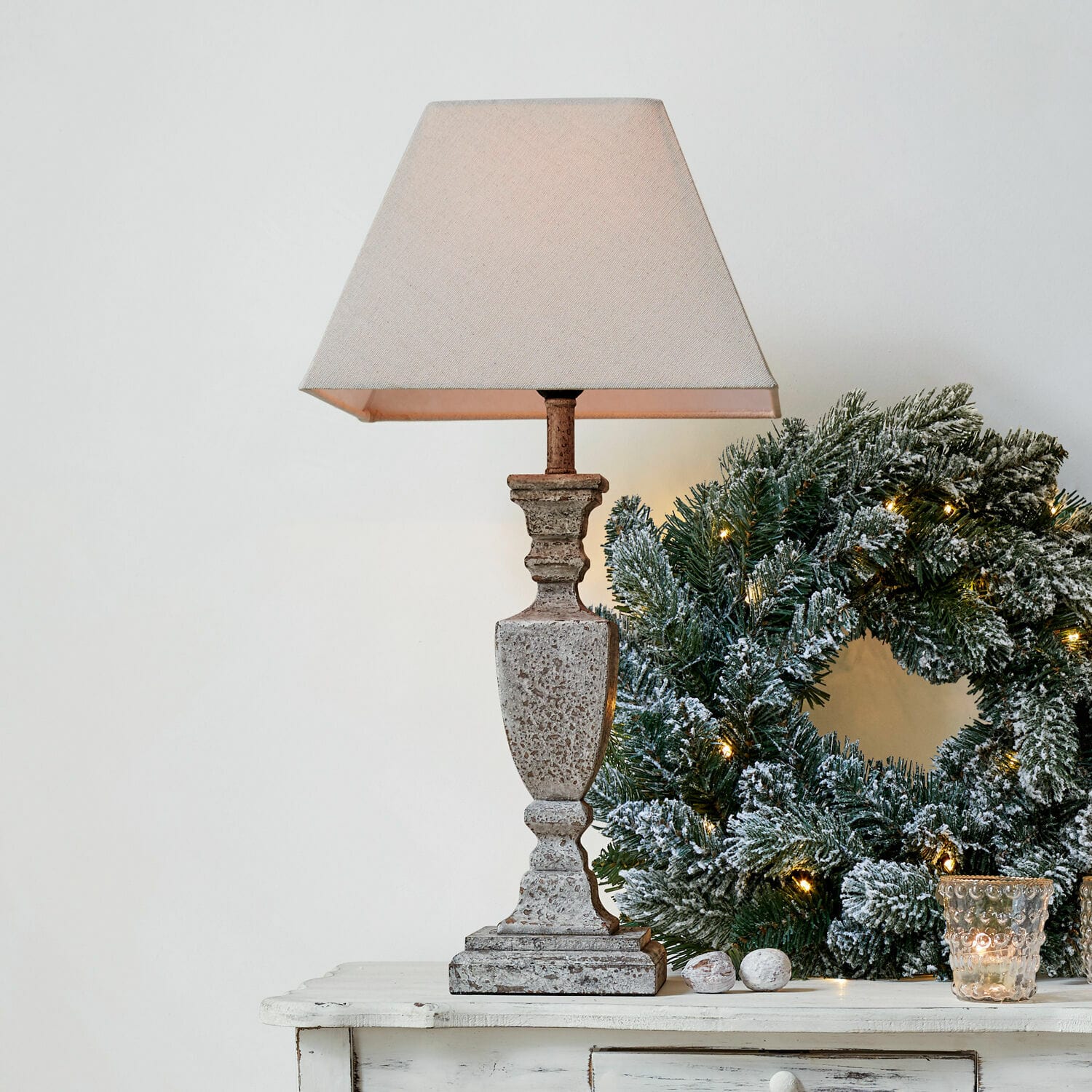 Tischlampe Gorham Beige Steintischlampe mit Lampenschirm neben grünem Weihnachtskranz mit Lichterkette auf weissem Tisch