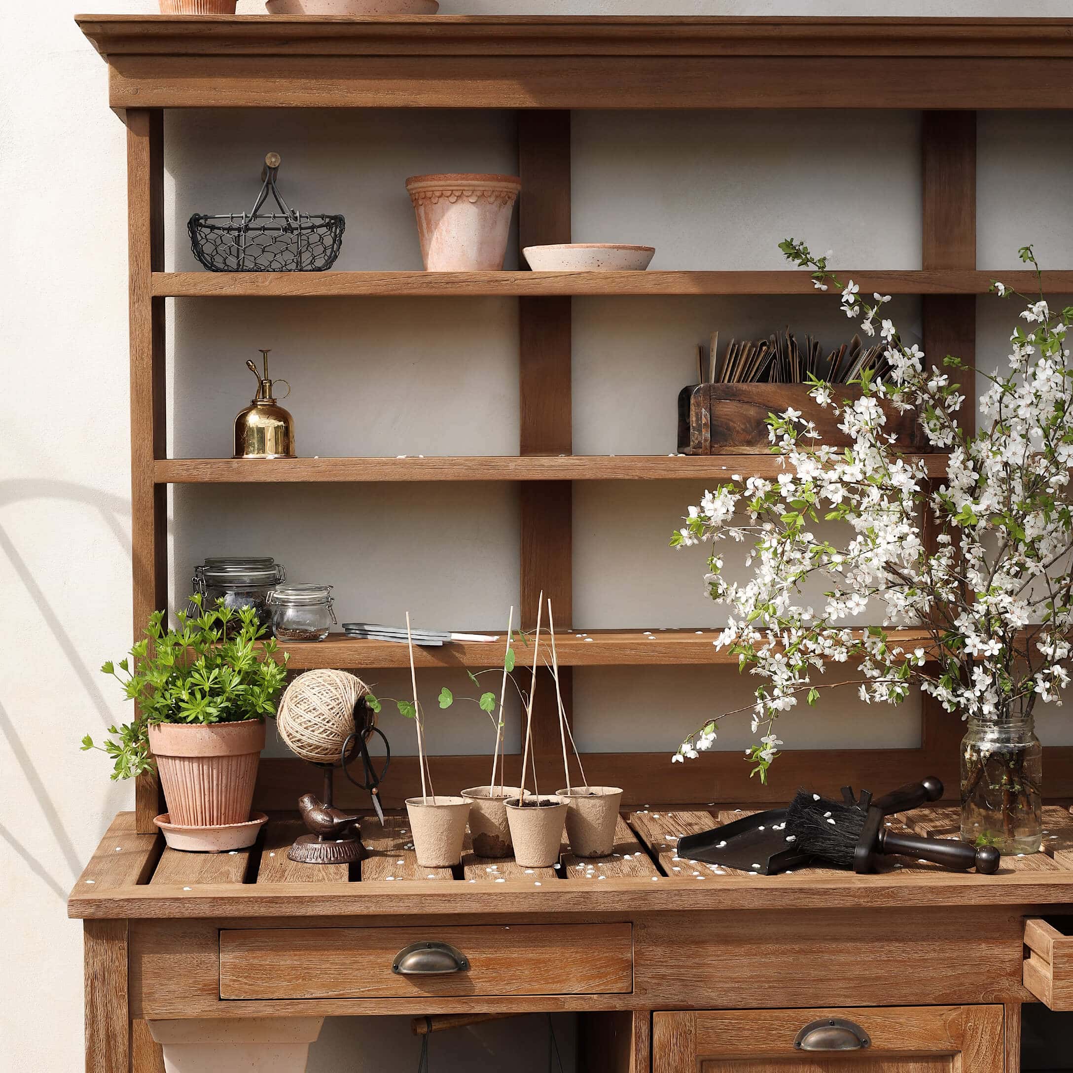Holz-Gartentisch mit Tontöpfen, Gartengeräten und blühenden Zweigen in Glasvase
