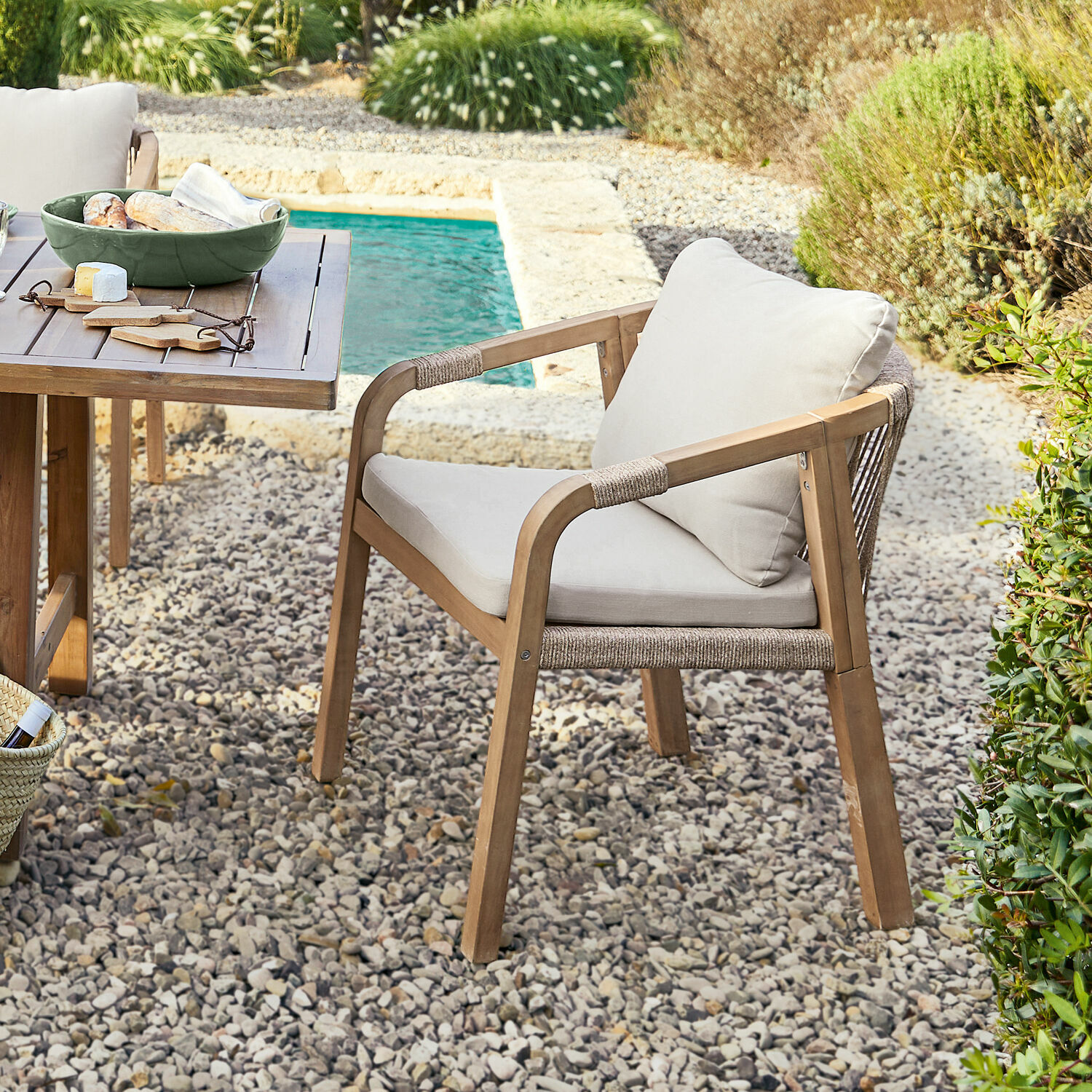 Gartenstuhl aus Holz mit hellen Polstern auf Kieselstein-Terrasse neben dem Pool