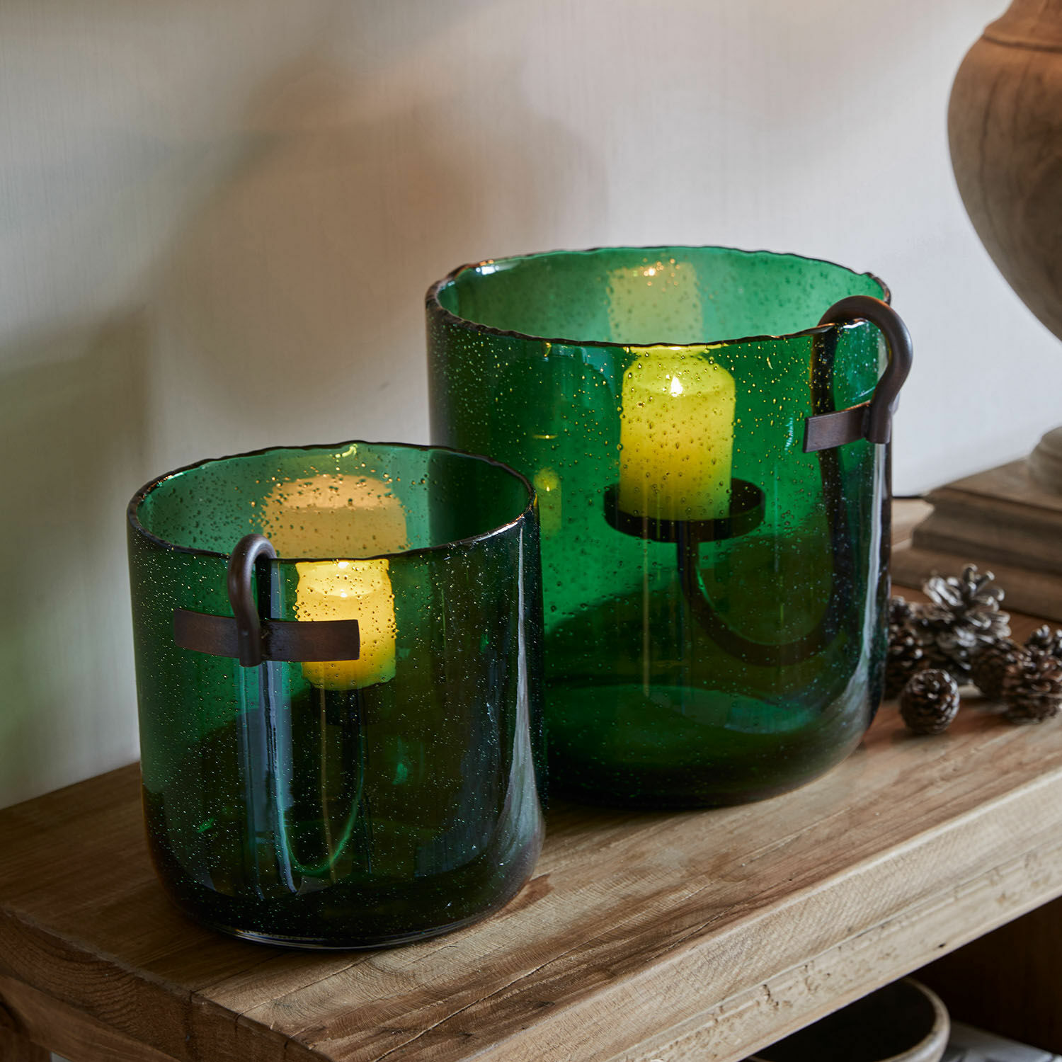 Set aus zwei grünen Glaswindlichtern mit Metallgriffen auf einem Holztisch