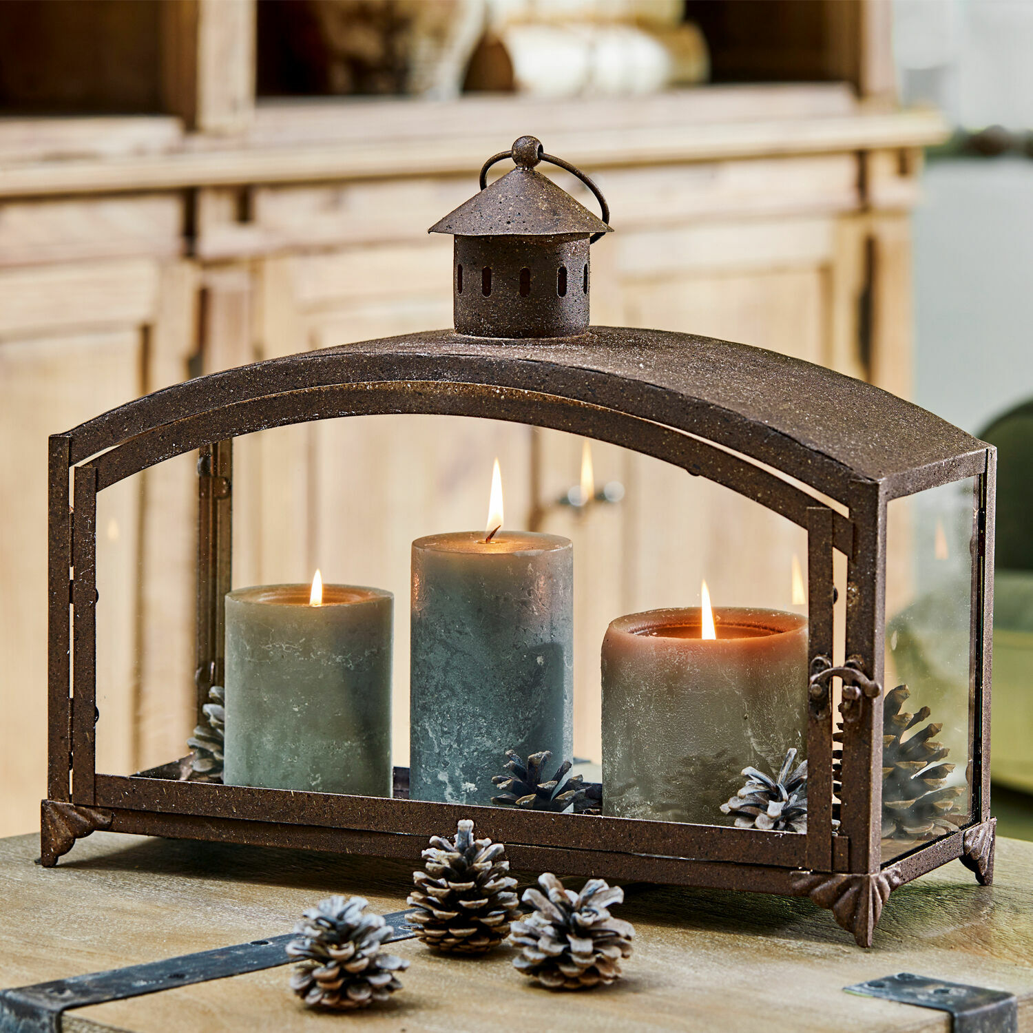 Metalllaterne mit drei grünen Kerzen und Kiefernzapfen auf Holztisch, Wohnraumdekoration