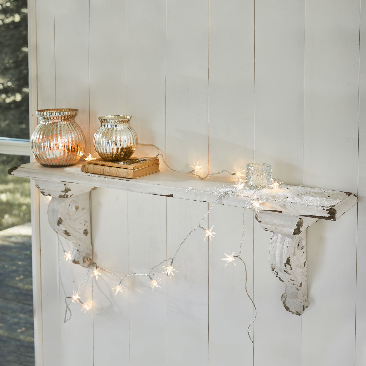 Wandregal Mouscron Weisse Holz-Wandkonsole mit Shabby-Chic-Effekt, dekoriert mit Stern-Lichterkette und Glaswindlichtern
