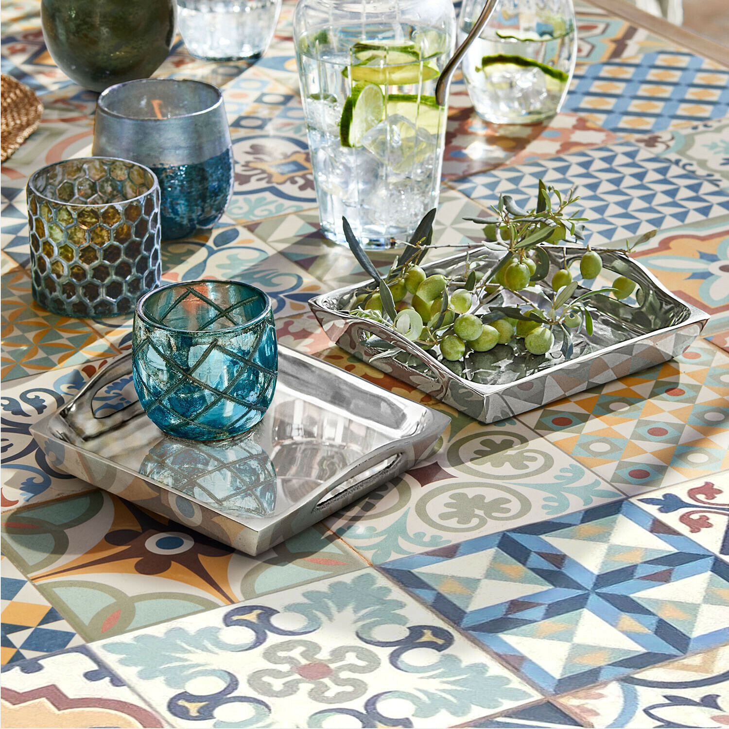 Tablett 2er Set Grélomiane Beidseitige silberne Metalltabletts auf buntem Mosaiktisch mit blauen Glaswindlichtern und grünen Oliven