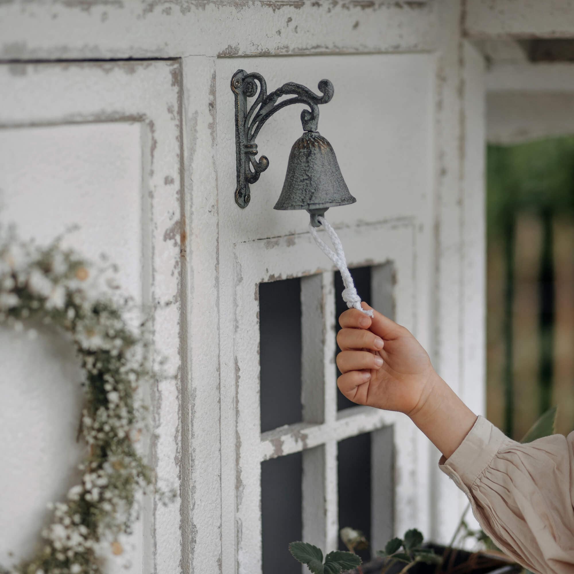 Metallglocke im Vintage-Stil mit weissem Seil an verwitterter Aussenwand montiert
