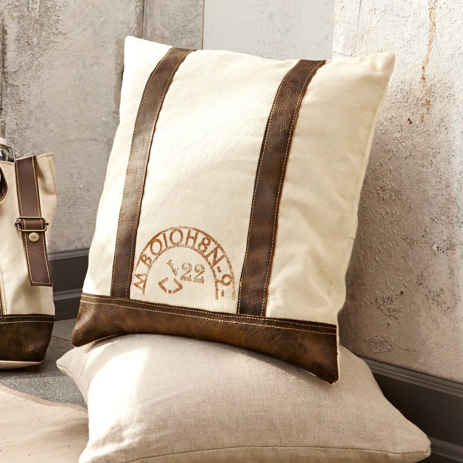 Beige Dekokissen mit braunen Lederstreifen und Vintage-Aufdruck für gemütliches Wohnen