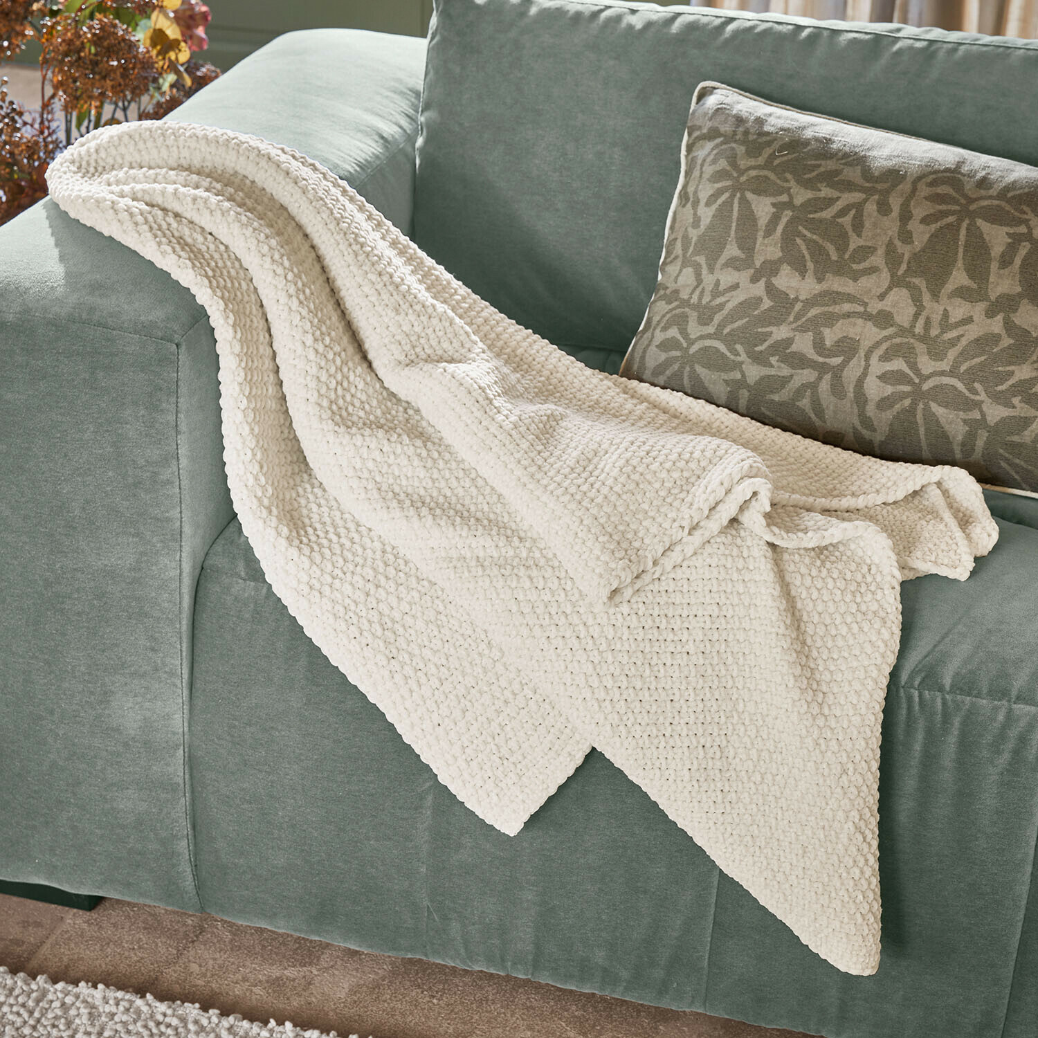 Plaid Linnet Weiche cremefarbene Strickdecke auf grünem Sofa, ideal für Wohnzimmer und Wohnaccessoires