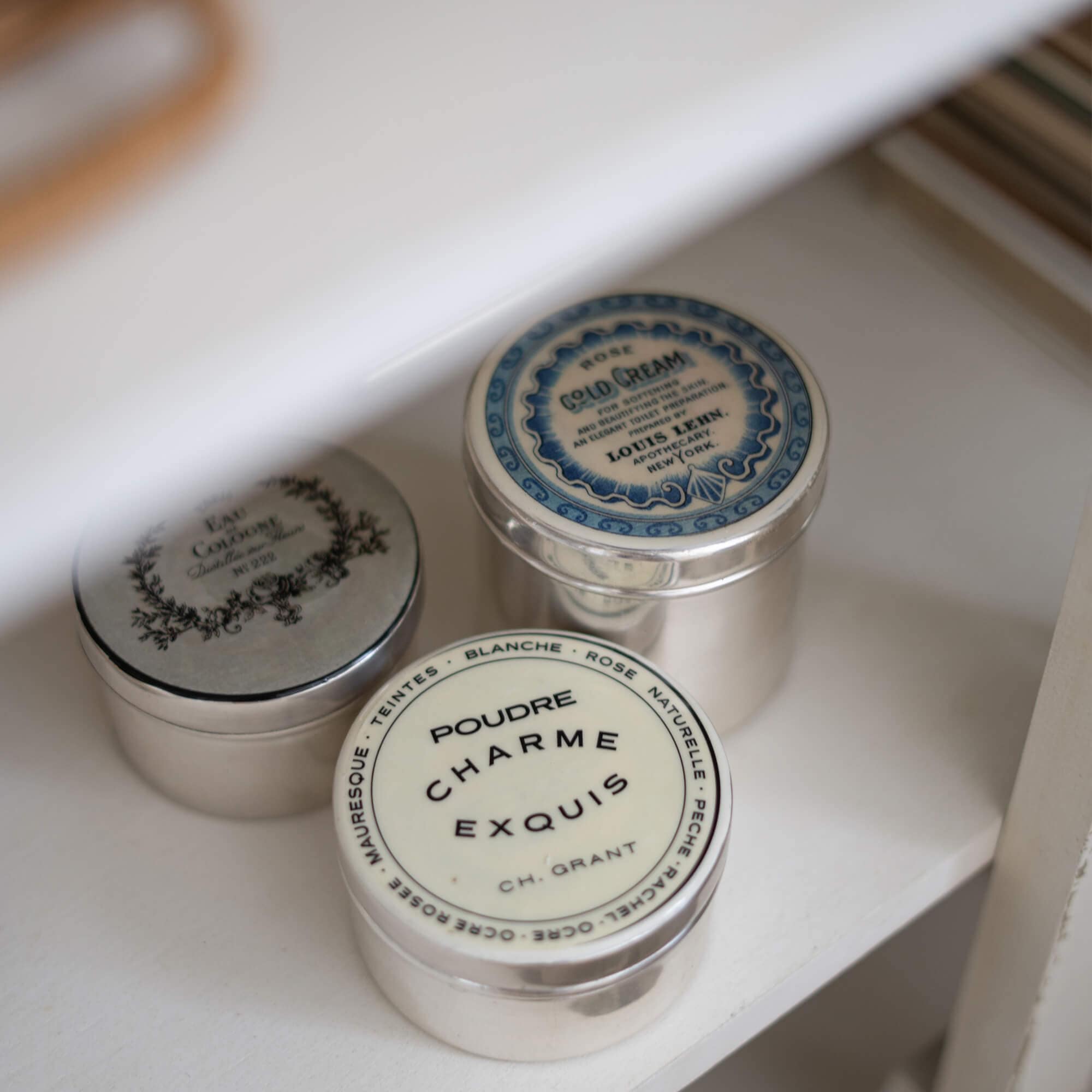 Drei metallene Vintage-Dosen mit Kosmetikaufklebern auf einem weissen Regal zur Aufbewahrung
