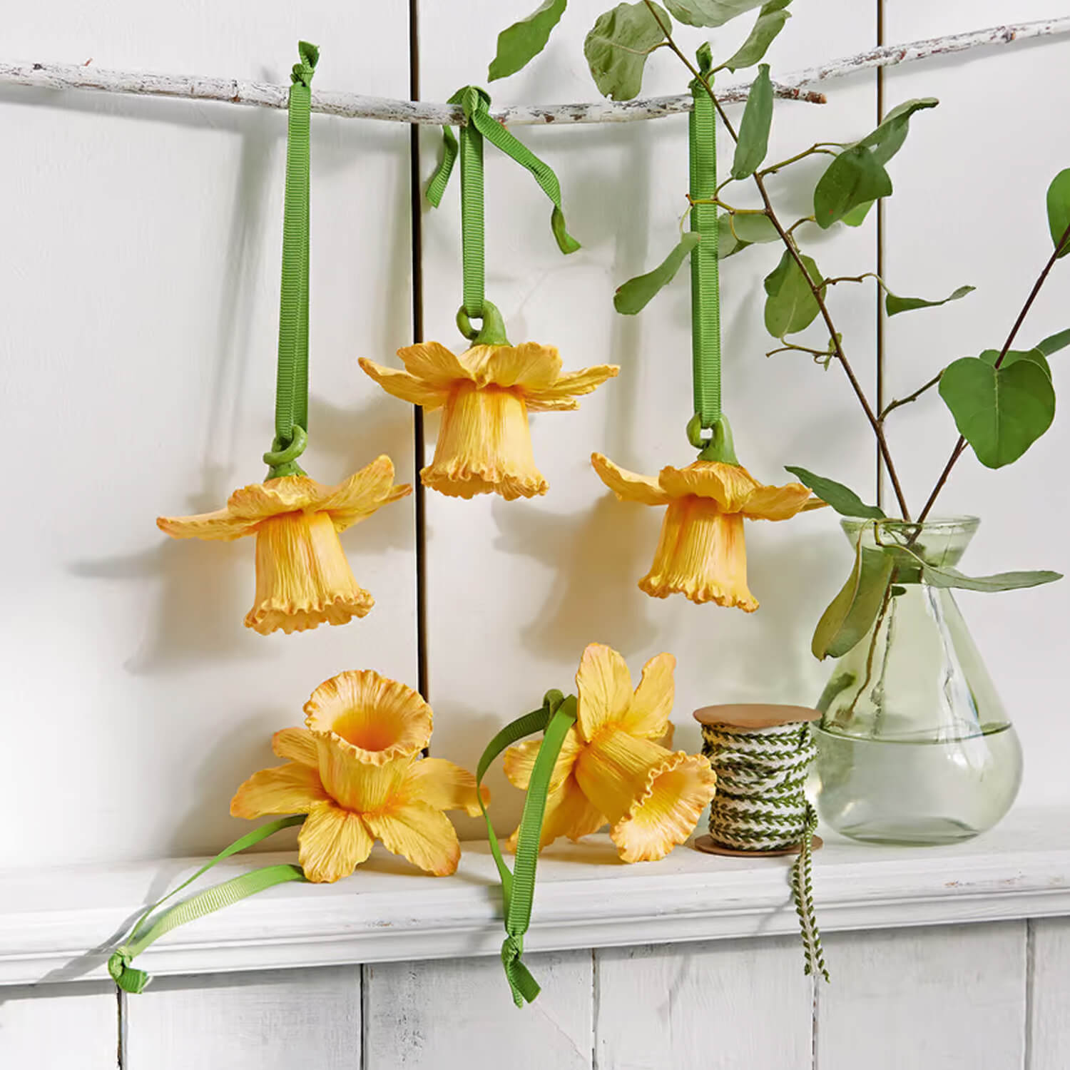 Gelbe Blumen-Dekorationen mit grünen Bändern an weissem Regal, Frühlingsdeko fürs Zuhause