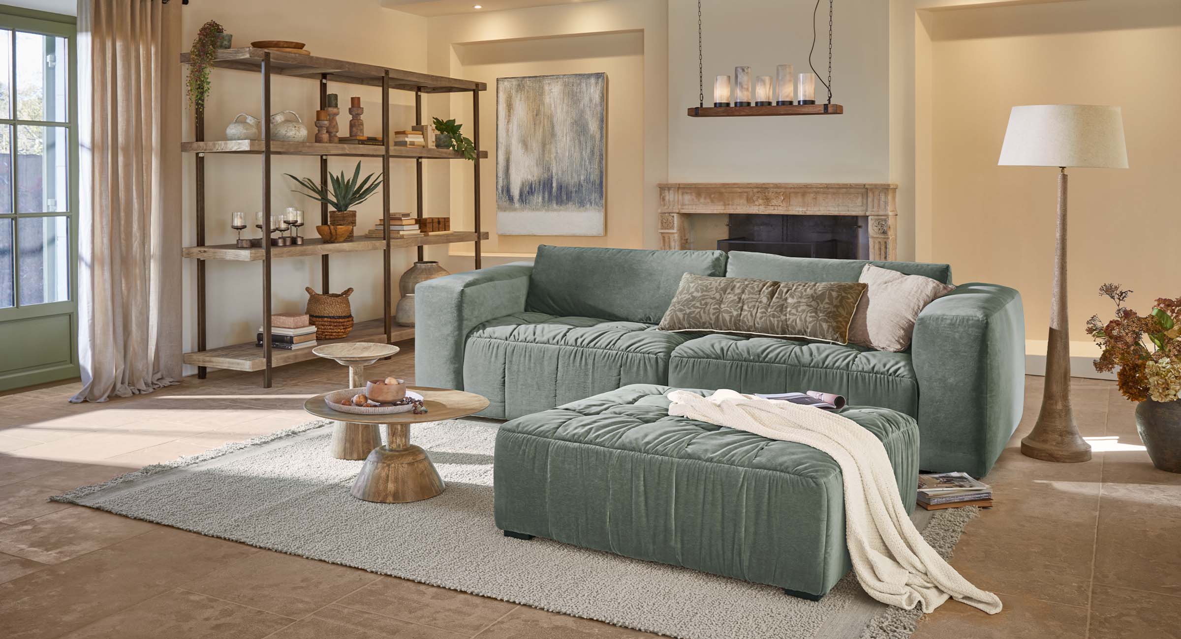 Grünes, weiches Sofa mit Hocker in hellem Wohnzimmer mit Holztischen und Regal