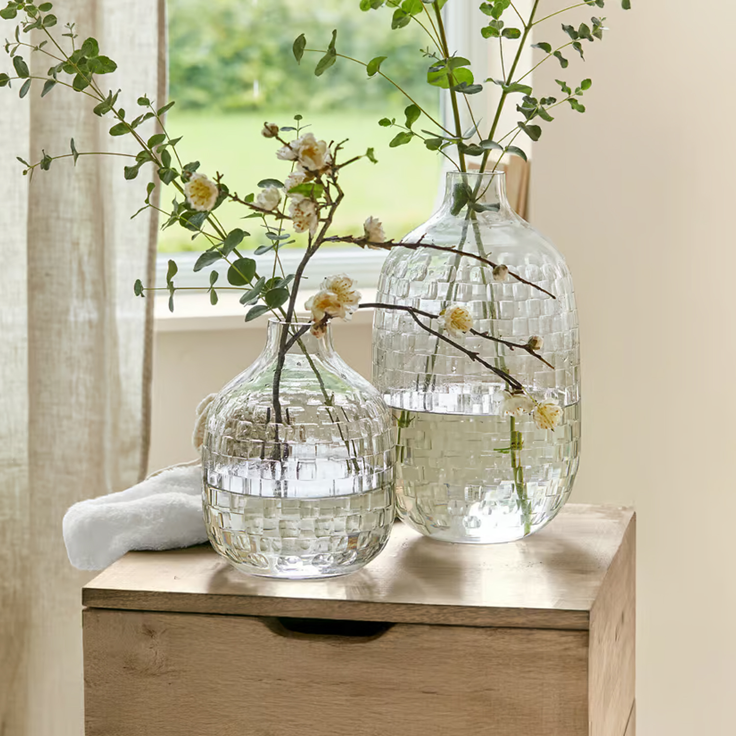 Transparente Glasvasen mit geometrischem Muster und Blumen auf Holztisch in hellem Raum