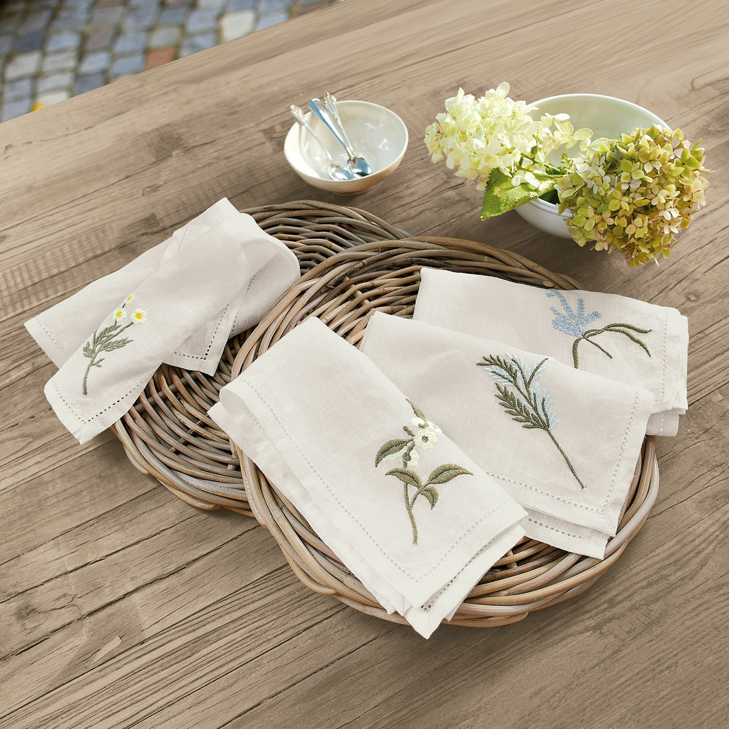 Serviette 4er Set Lentilly Leinenservietten mit pflanzlicher Stickerei in Naturfarbe auf einem Weidenkorb auf Holztisch