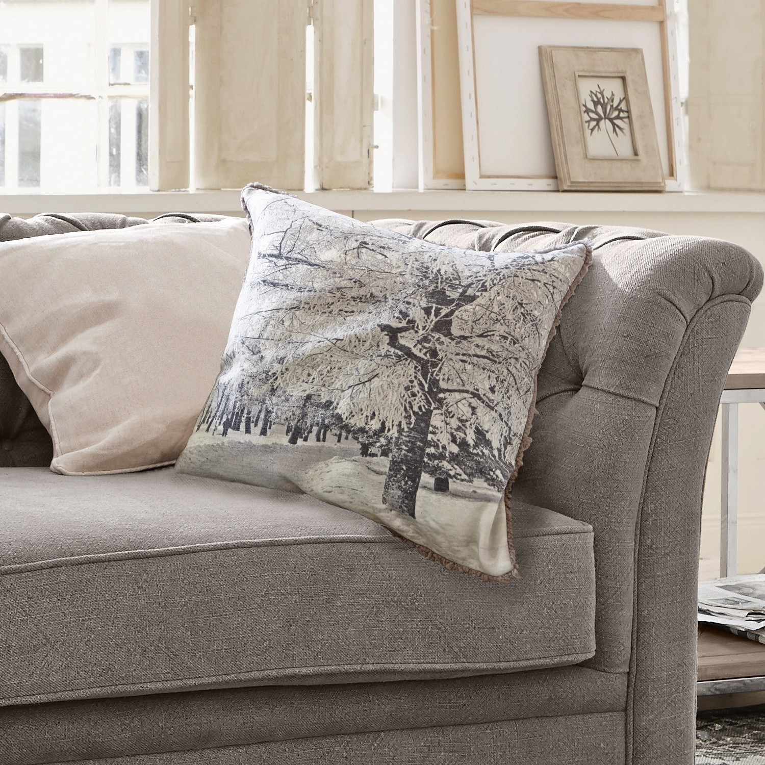 Graues Sofa mit zwei Kissen, eines mit Winterbaum-Motiv, gemütliche Wohnzimmerdekoration