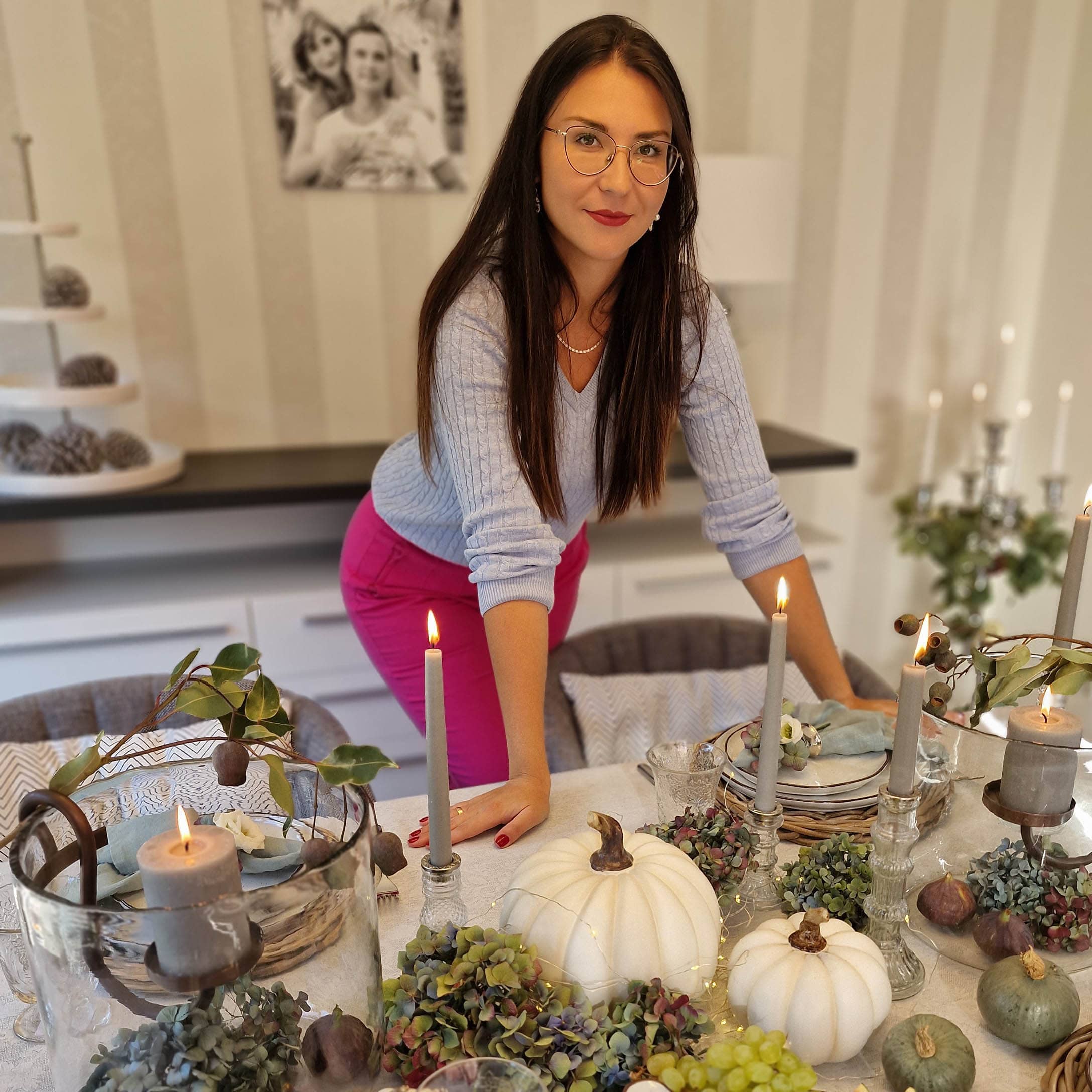 Frau an einem Tisch mit herbstlicher Dekoration aus weissen Kürbissen, Kerzen und grünen Blumen im Raum.