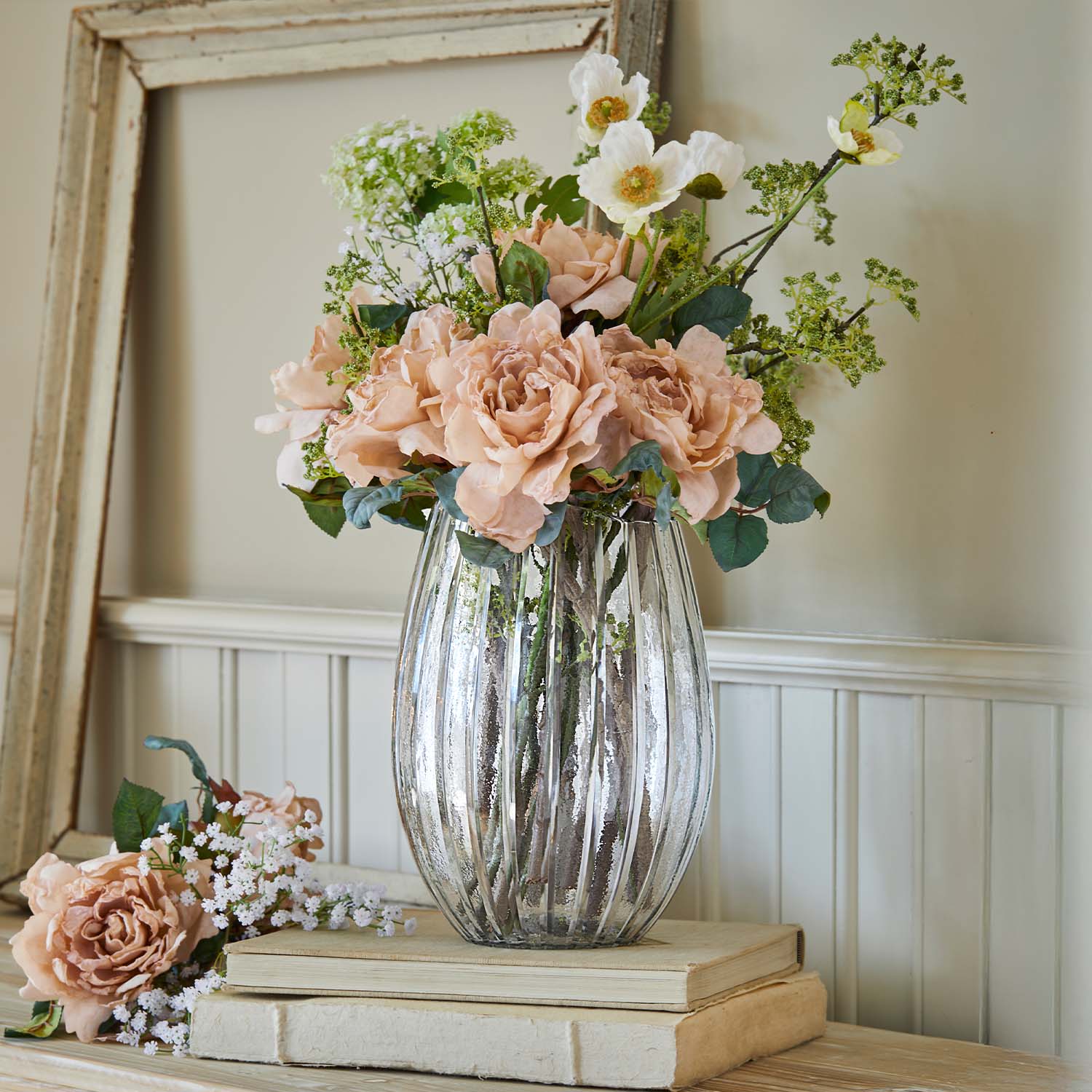 Glasvase mit geriffeltem Glas und Strauß aus beigen Rosen und weißen Dekoblumen auf Büchern