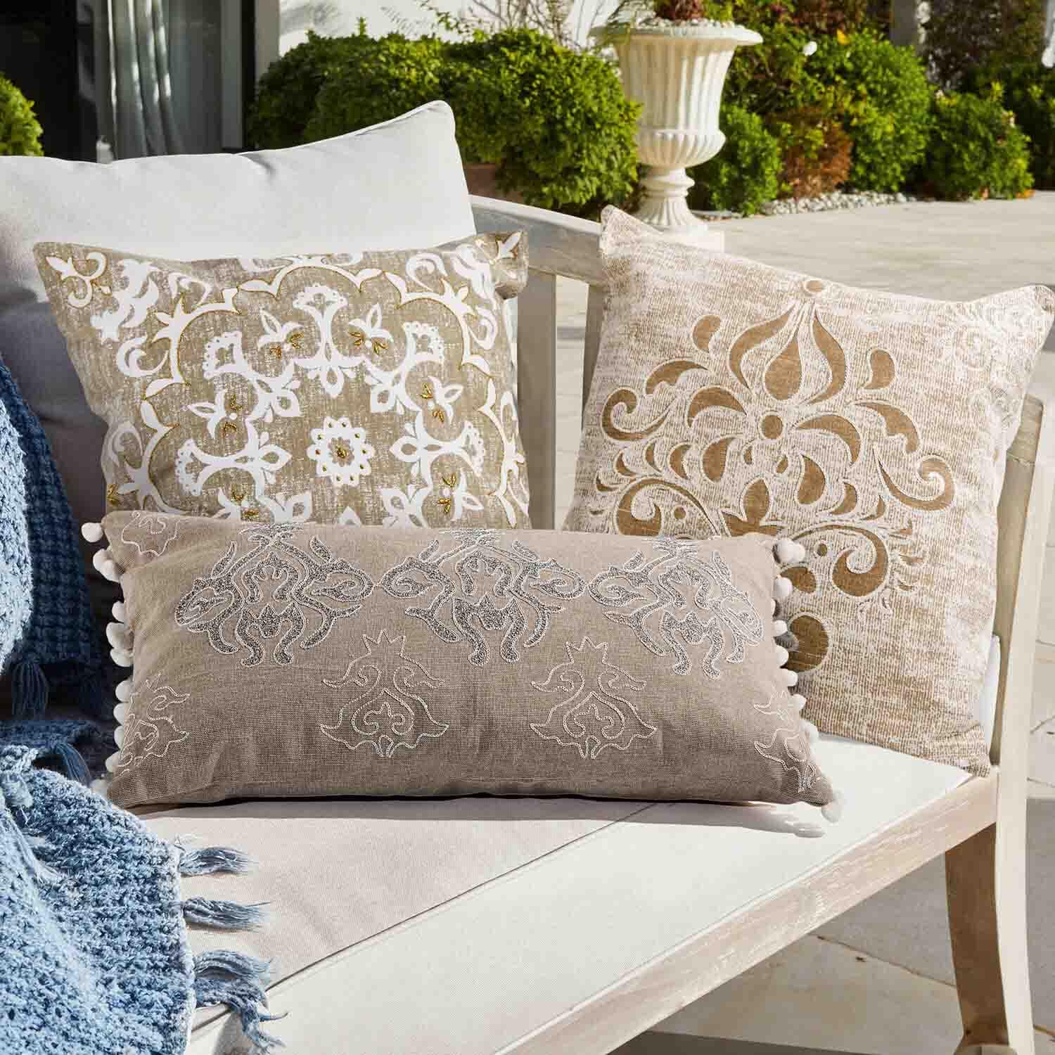 Drei dekorative Kissen in Beige und Weiss mit Mustern auf hellem Sofa im Garten