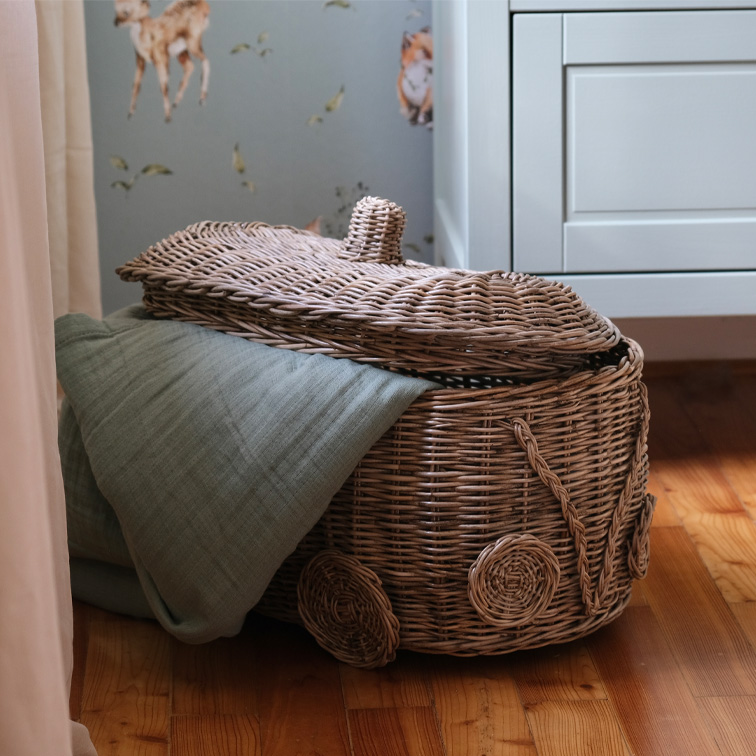Wiklinerkorb in Autoform mit grünem Tuch auf Holzboden im Kinderzimmer
