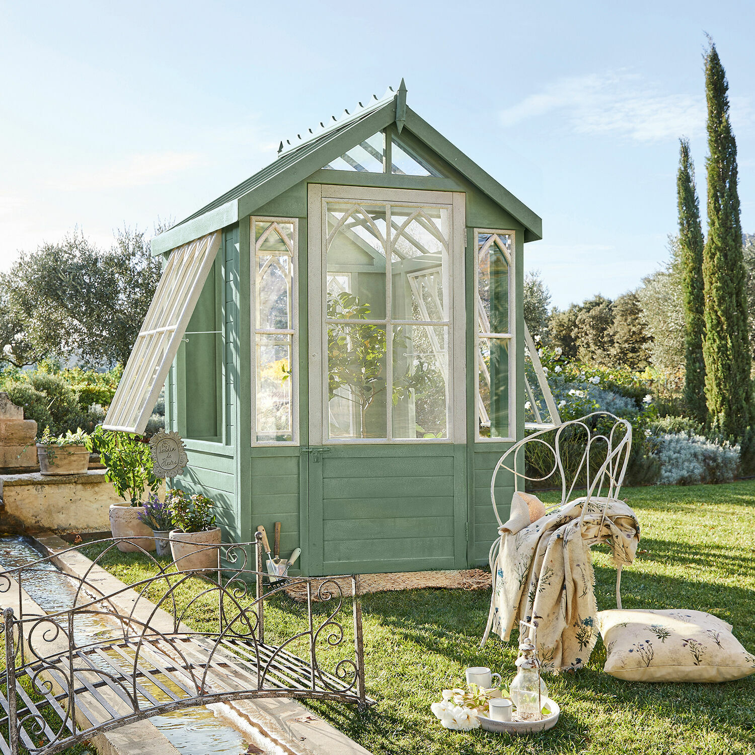 Gartenhaus Anyós Grünes Holzgewächshaus mit weissen Fenstern und Metallmöbeln auf dem Rasen im Garten