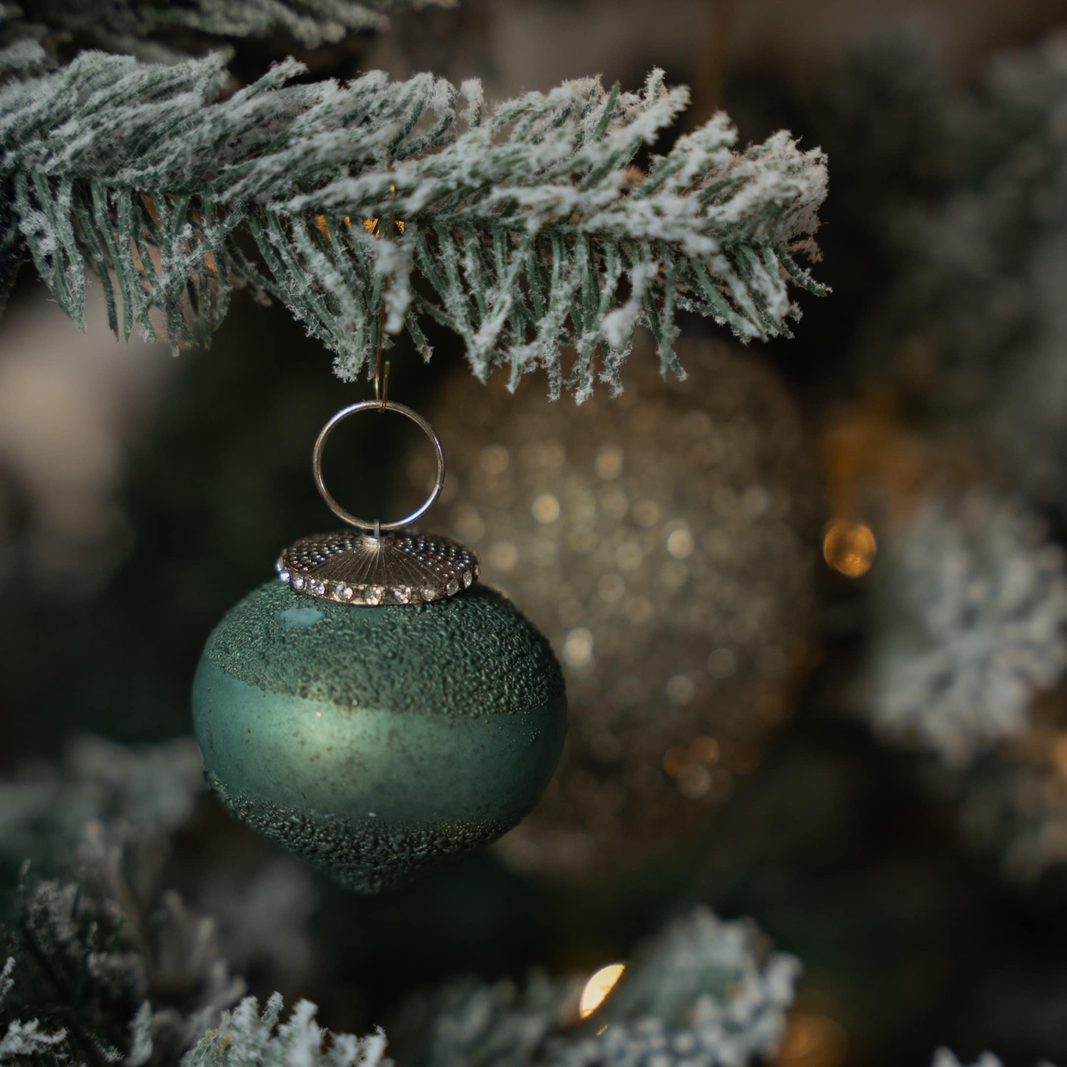 Grüne matte Weihnachtskugel mit strukturierter Oberfläche und silberner Aufhängung an verschneitem Zweig