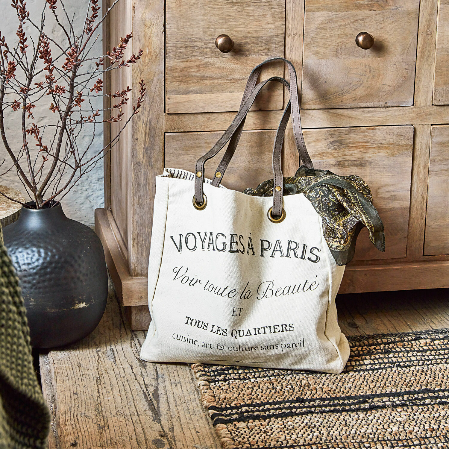 Tasche Voyage Beige Baumwolltasche mit schwarzem Druck und braunen Griffen auf Holzboden