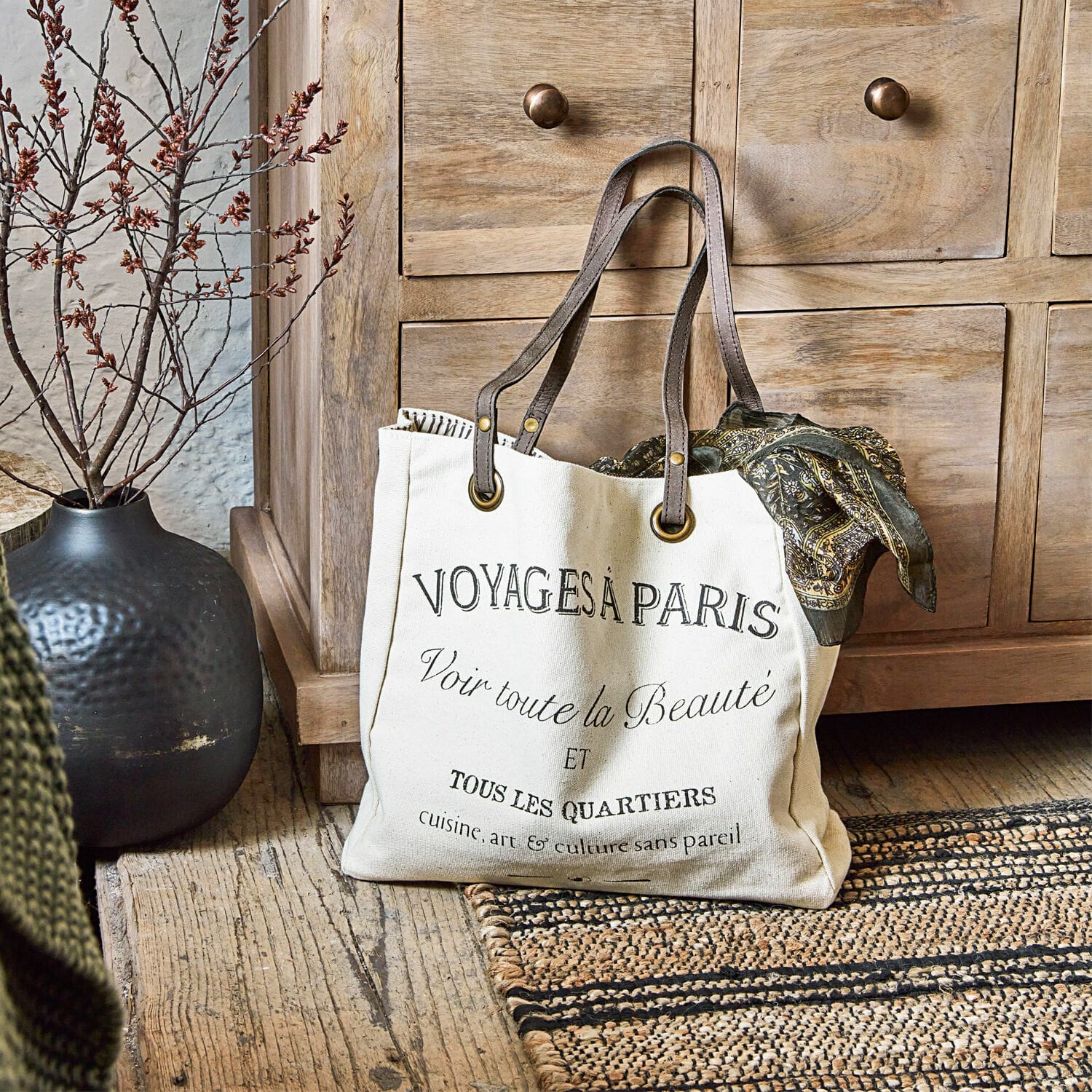 Tasche Voyage Beige Baumwolltasche mit schwarzem Druck und braunen Griffen auf Holzboden