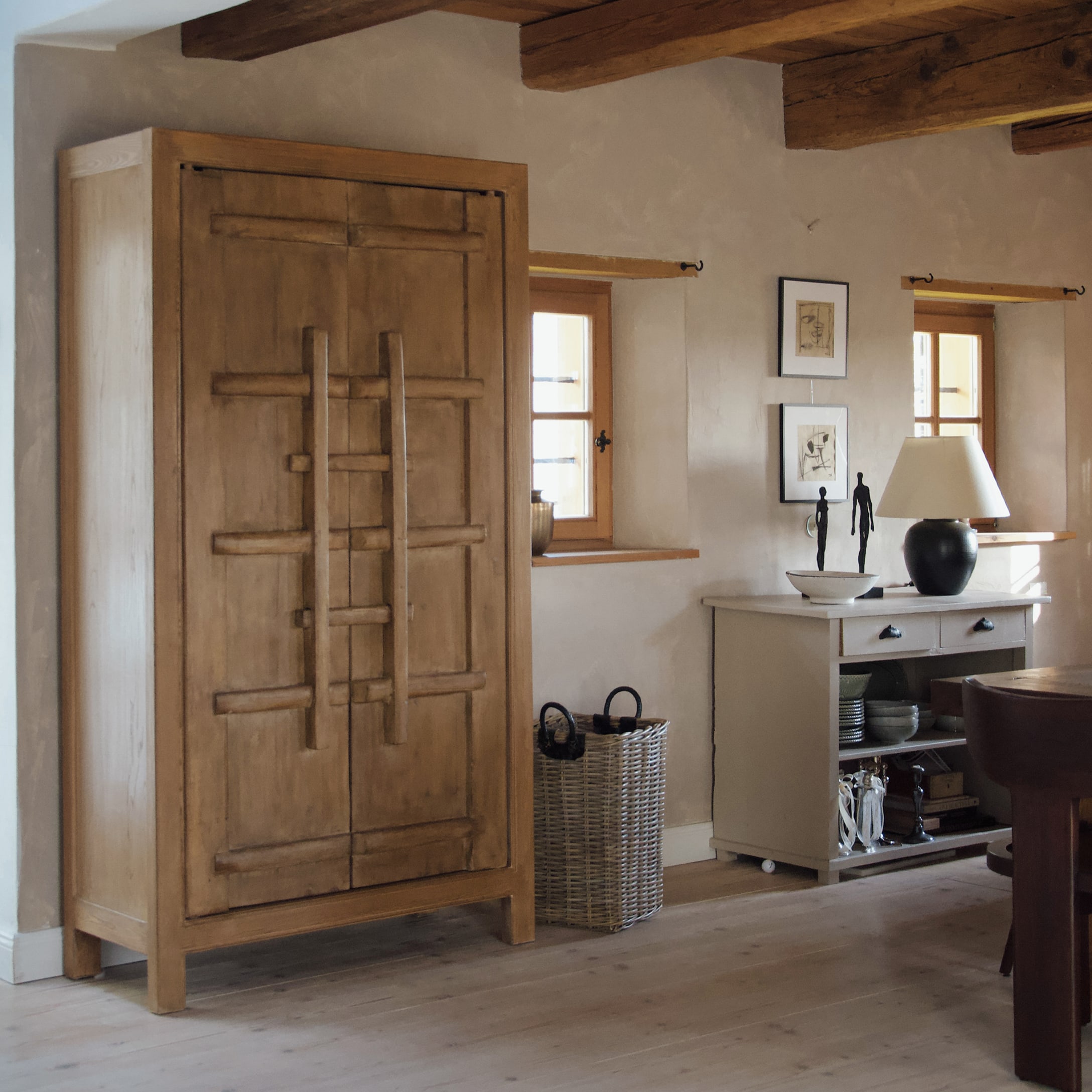 Holzschrank in Naturfarbe in rustikalem Raum mit Korb aus Weide und weissem Sideboard