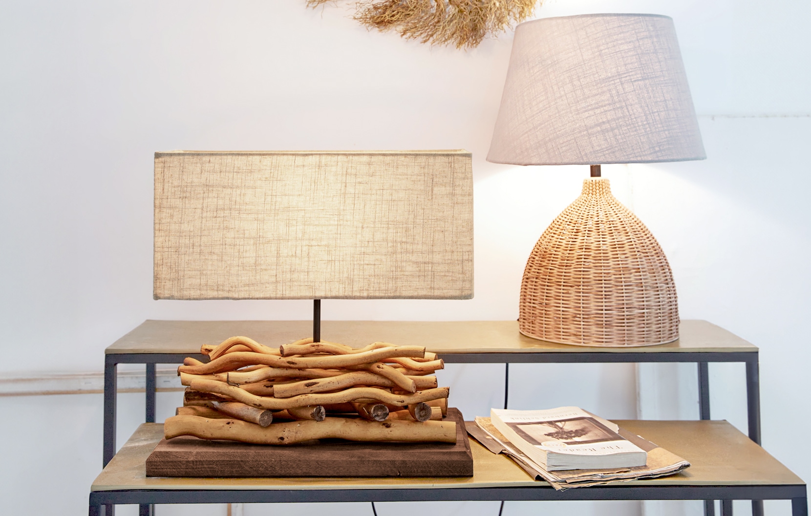 Zwei Tischlampen aus Naturholz und Korbgeflecht mit beigen Lampenschirmen auf einem Metalltisch