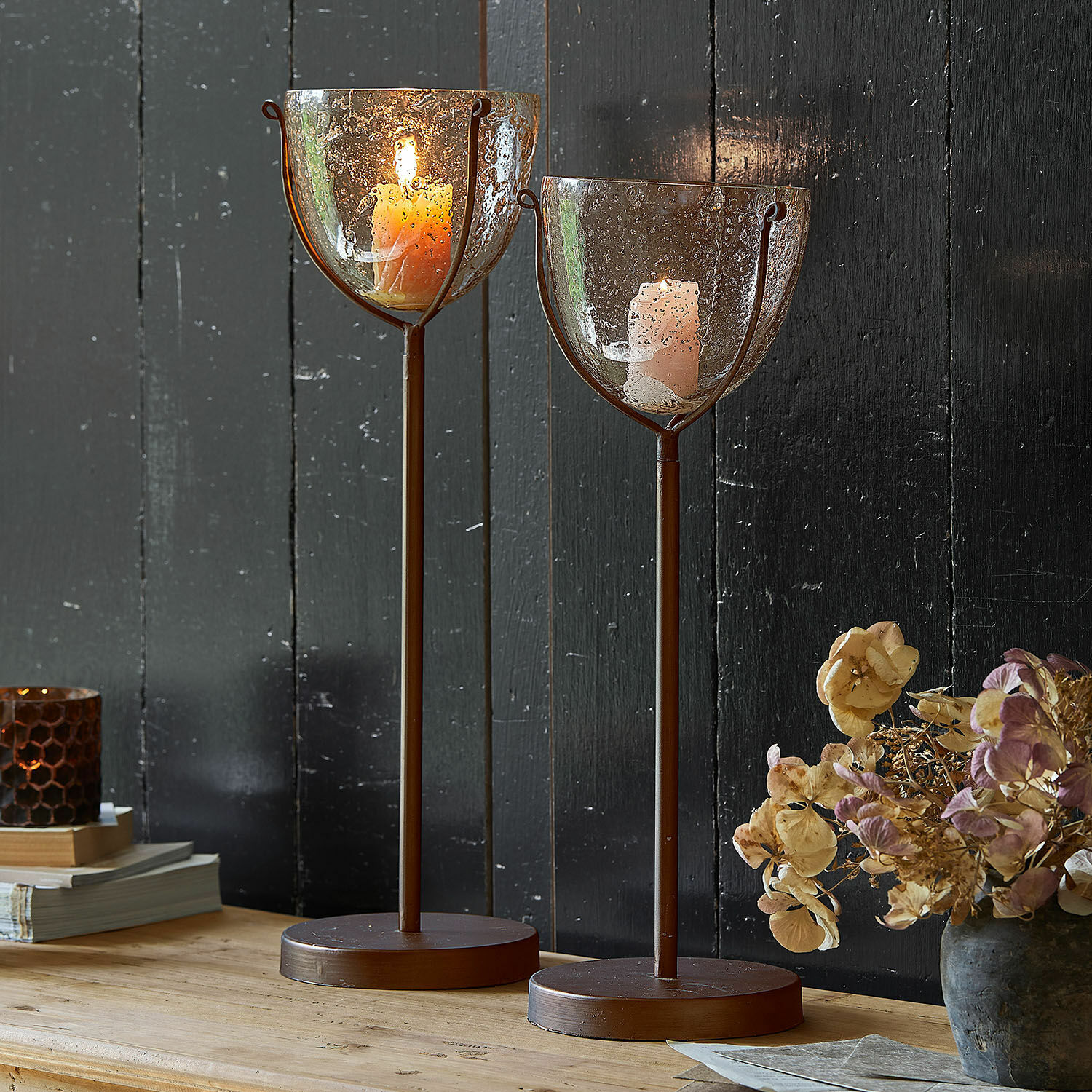 Kerzenständer 2er Set Piacello Zwei braune Metallkerzenhalter mit geblasenem Glas und brennenden Kerzen auf Holztisch