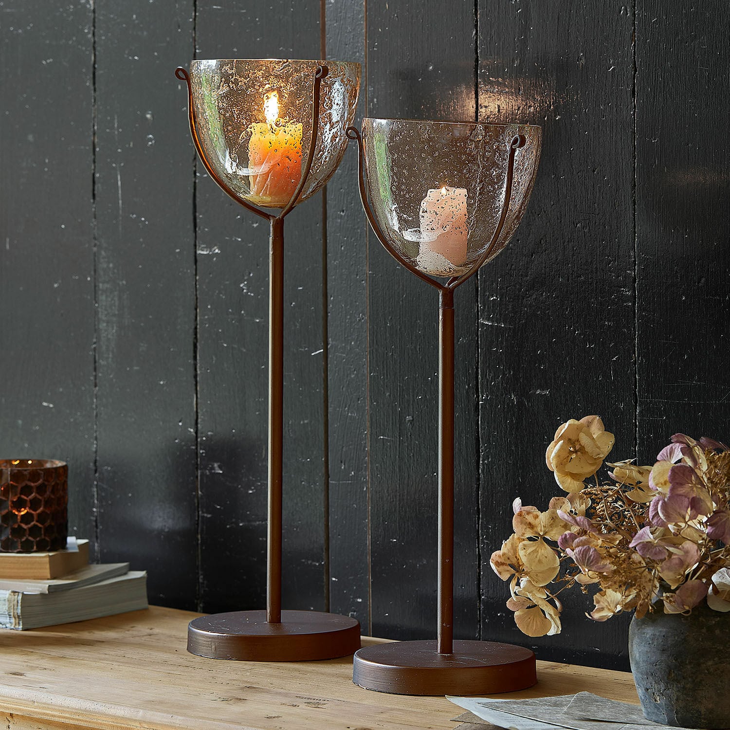 Kerzenständer 2er Set Piacello Zwei braune Metallkerzenhalter mit geblasenem Glas und brennenden Kerzen auf Holztisch