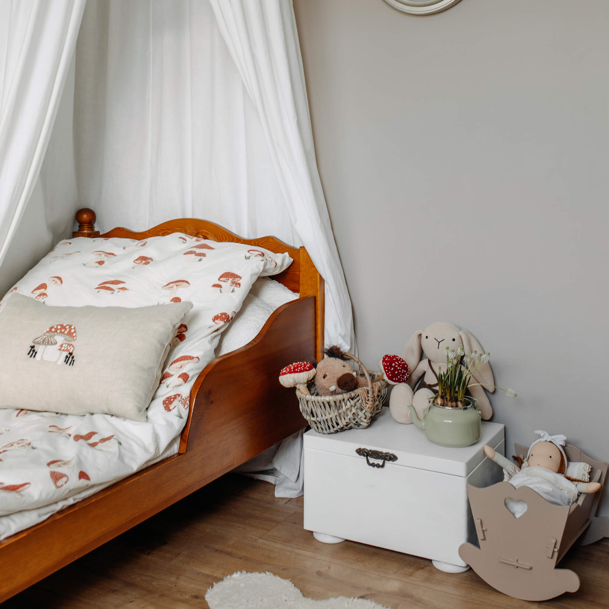 Kinderbett aus Holz mit weisser Bettwäsche mit Pilzmotiv und Kuscheltieren auf weisser Truhe
