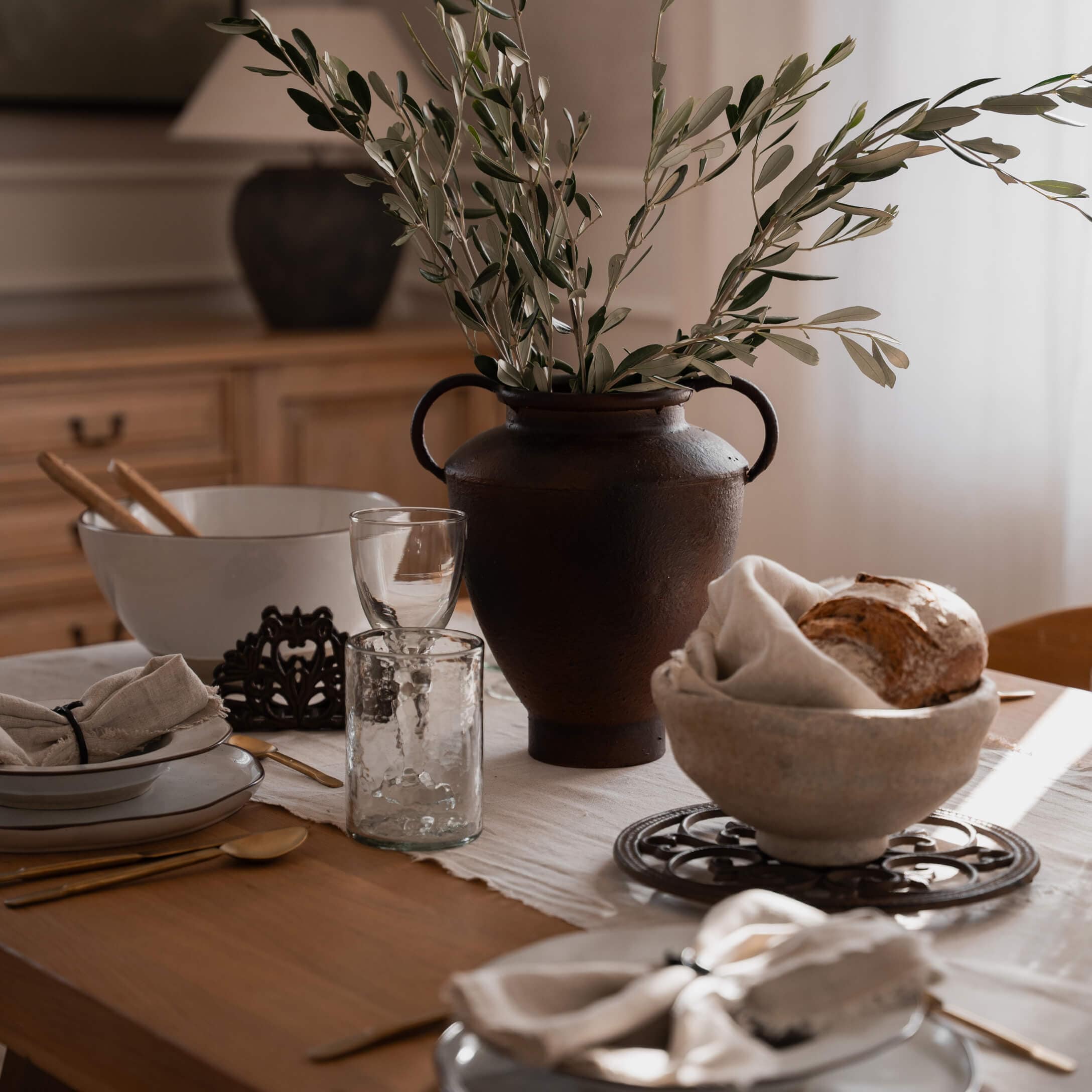 Rustikale braune Keramikvase mit grünen Zweigen auf Holztisch mit Geschirr