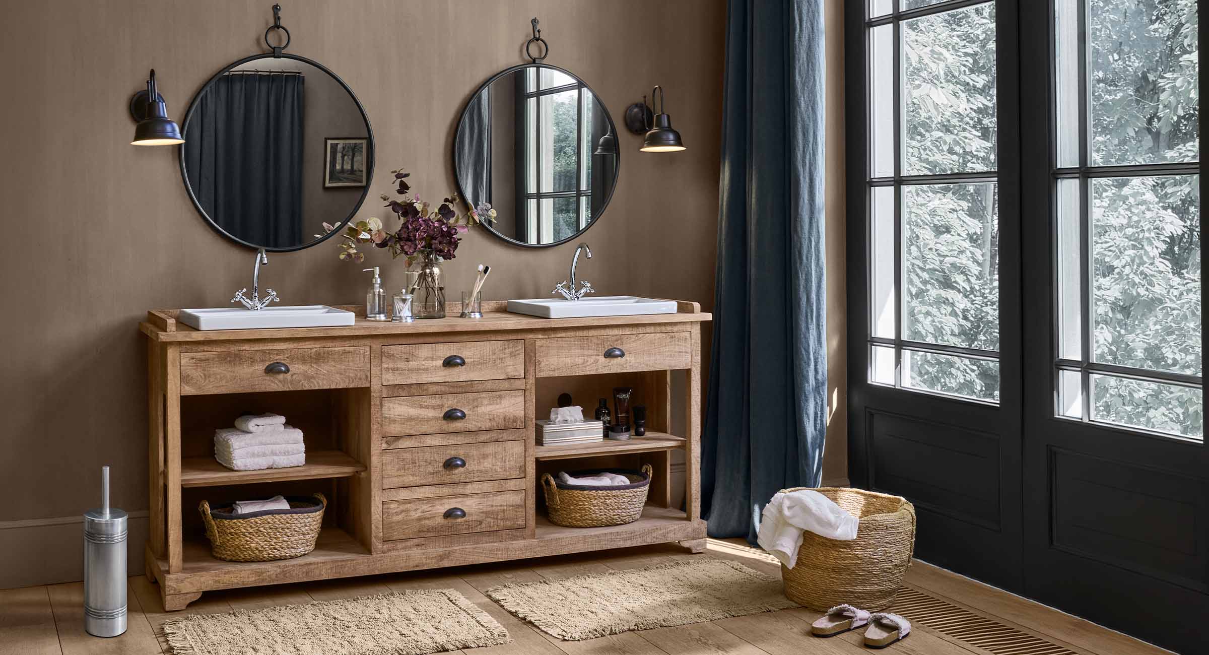 Holz-Badezimmerschrank mit zwei weissen Waschbecken und runden Spiegeln in natürlichem Ambiente