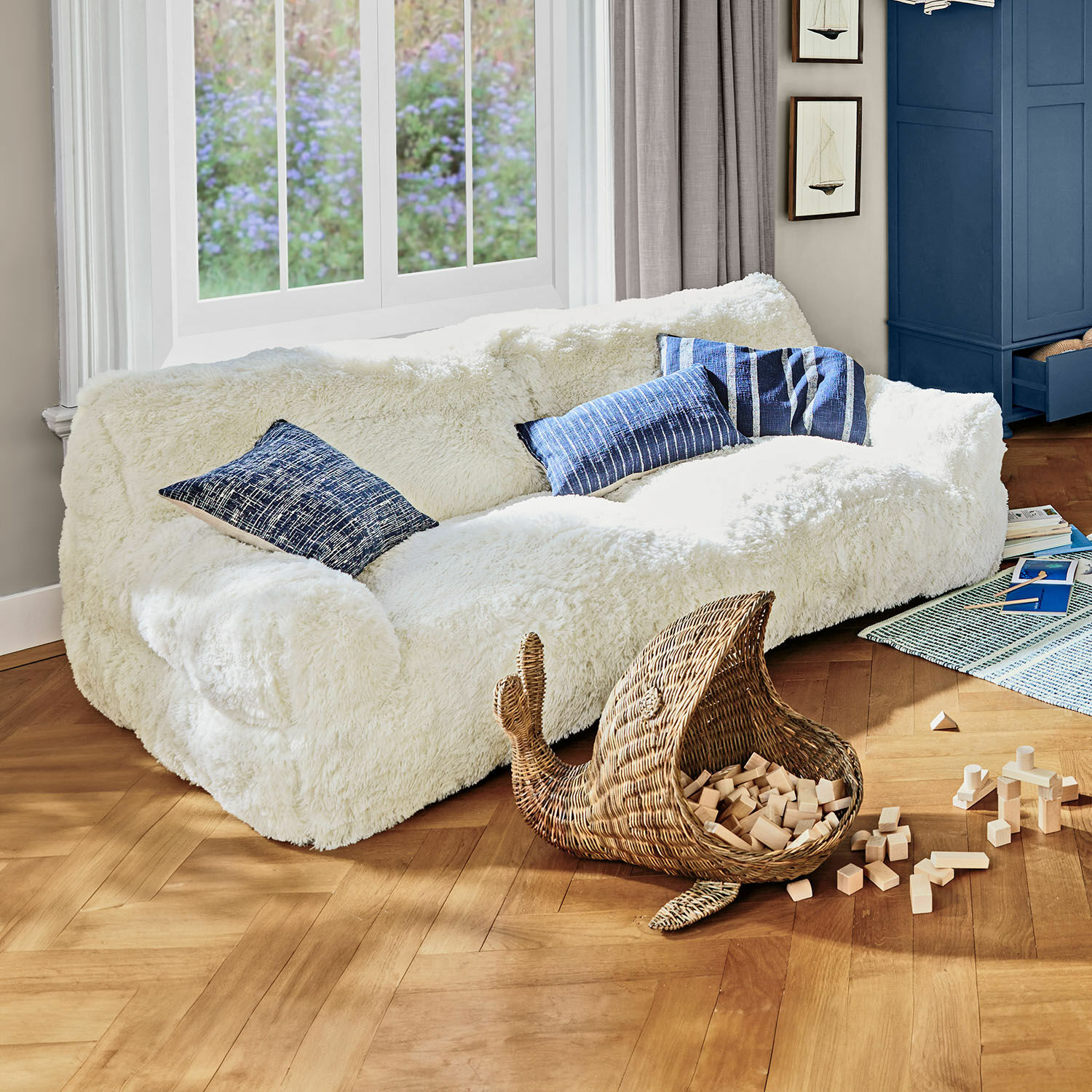 Kindersofa Cerveteri Weisses, flauschiges Sofa mit blauen Kissen in hellem Wohnzimmer mit Holzparkett